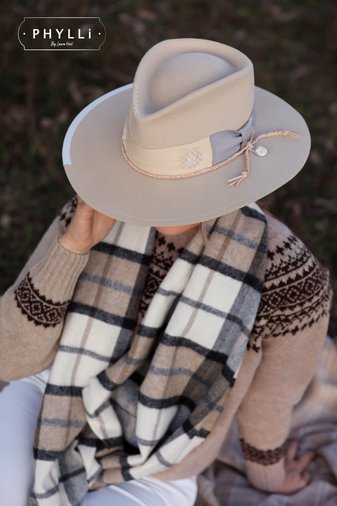 Woman wearing Fallon beige rabbit felt hat by PHYLLi Designs sitting outdoors with plaid scarf and neutral winter styling.