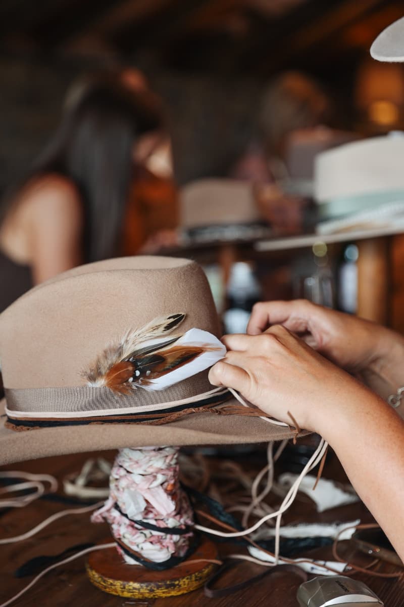 Close up detail of a PHYLLi felt hat showing fallen feather bunch tucked into a grosgrain hat band during in-studio trimming.