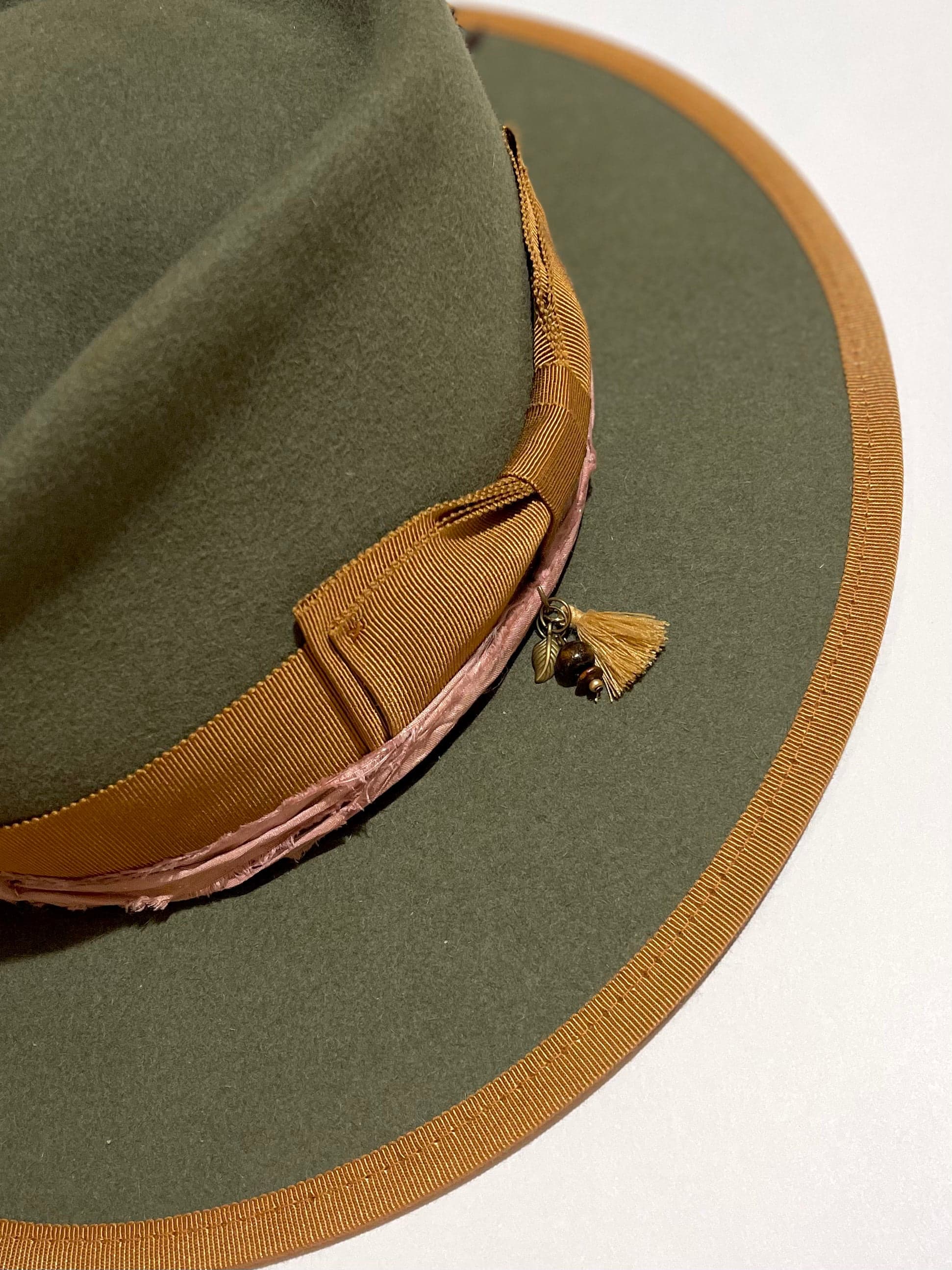 Close up of charm cluster with tassel, bronze leaf charm and timber bead on the Feuille Morte felt hat by PHYLLi Designs.