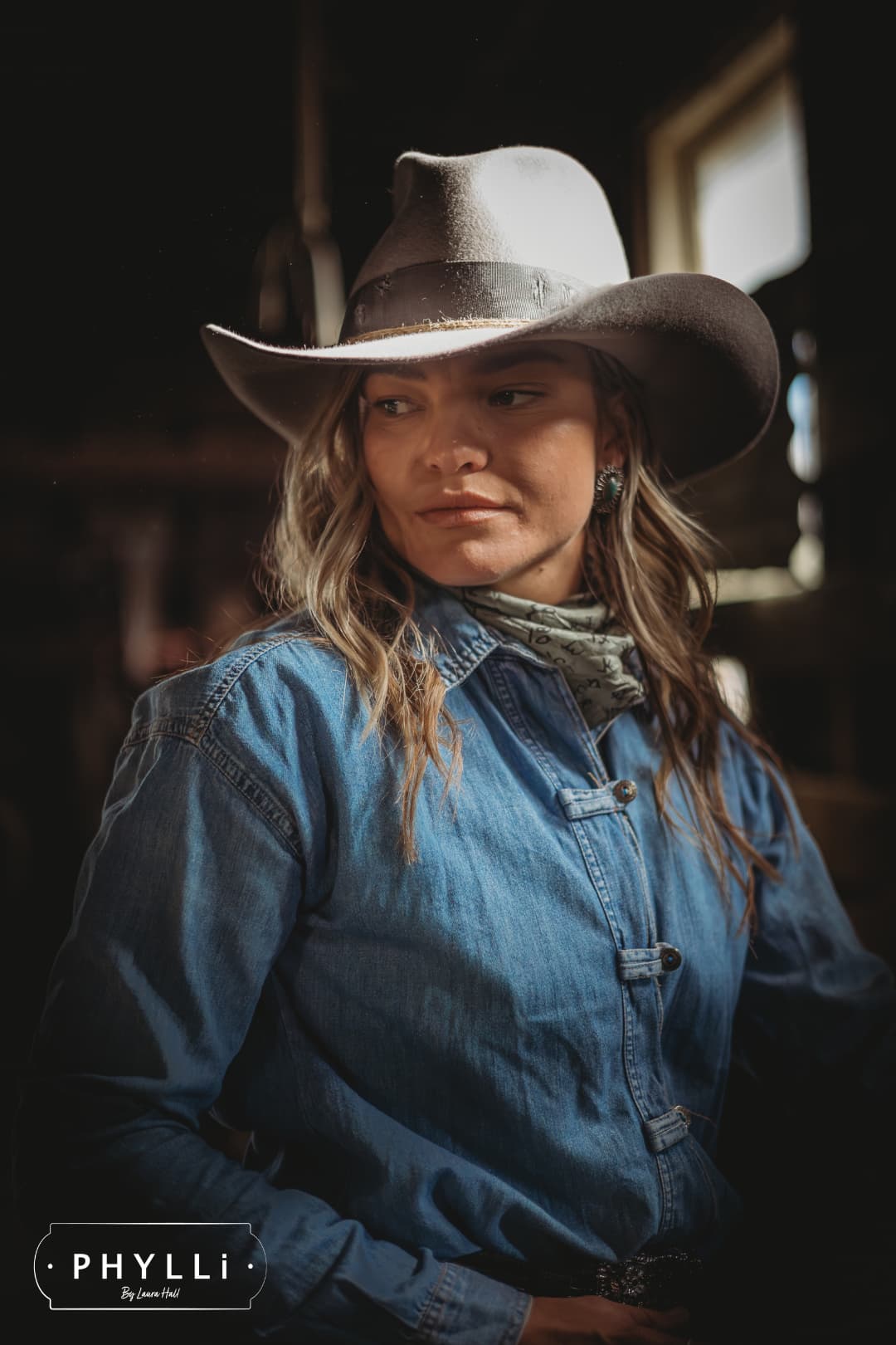 Female model wearing the Finse cement felt cowboy hat by PHYLLi Designs with turquoise beaded twine wraps in a rustic barn interior.