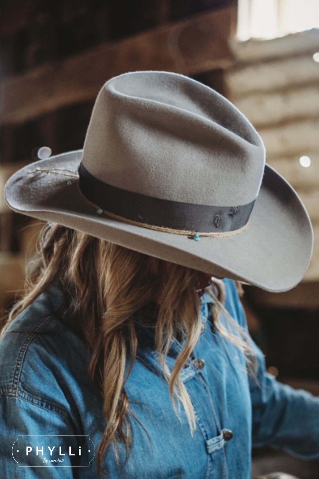 Close up model wearing the Finse cement felt cowboy hat by PHYLLi Designs with distressed steel grey grosgrain band in a rustic stable setting.