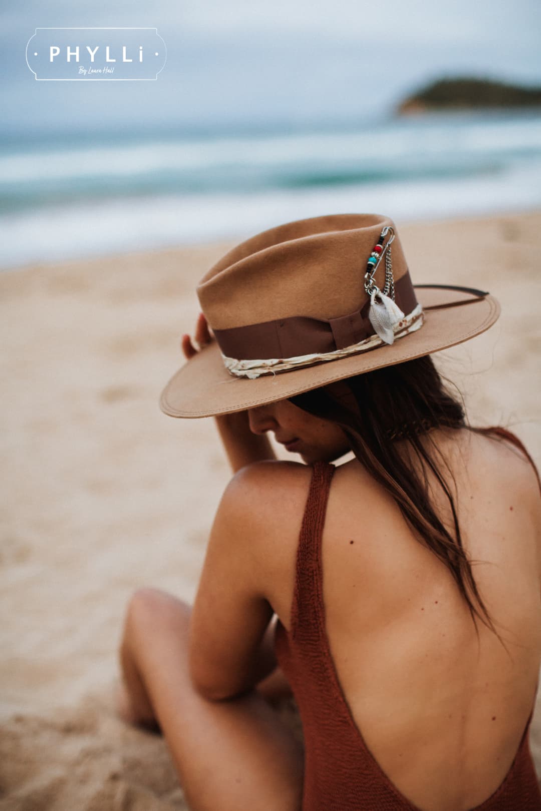 Close-up of woman wearing Fly Fisher camel felt hat by PHYLLi Designs on the beach showing silver chunky hat pin with feathers and chains.