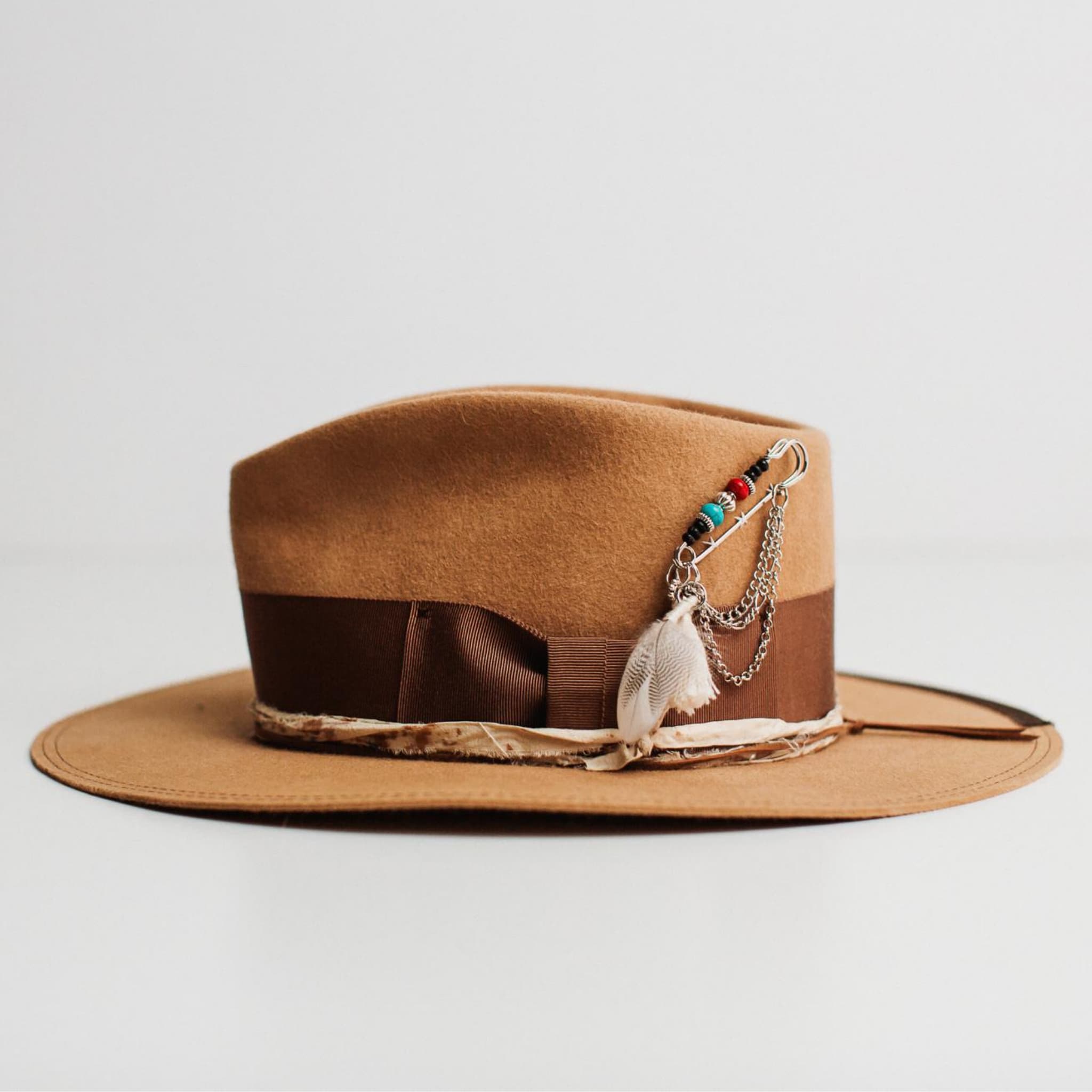 Left side view of Fly Fisher camel felt hat by PHYLLi Designs with chocolate grosgrain band, dark brown brim trim and silver chunky hat pin with feathers and chains.