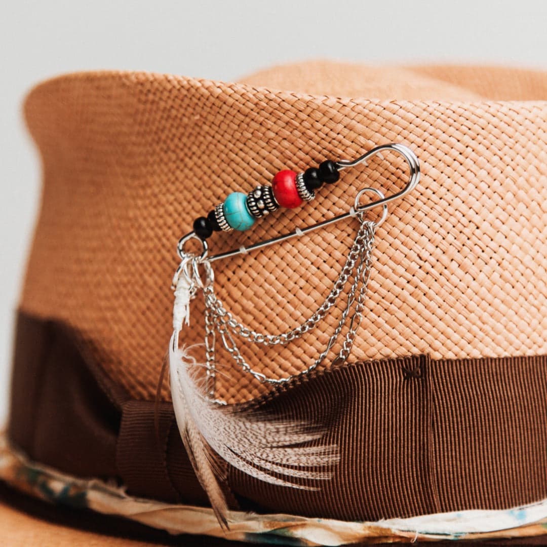 Close up detail of the Fly Fisher Panama hat showing chunky silver hat pin with turquoise bead, feather, chains and beaded detailing.