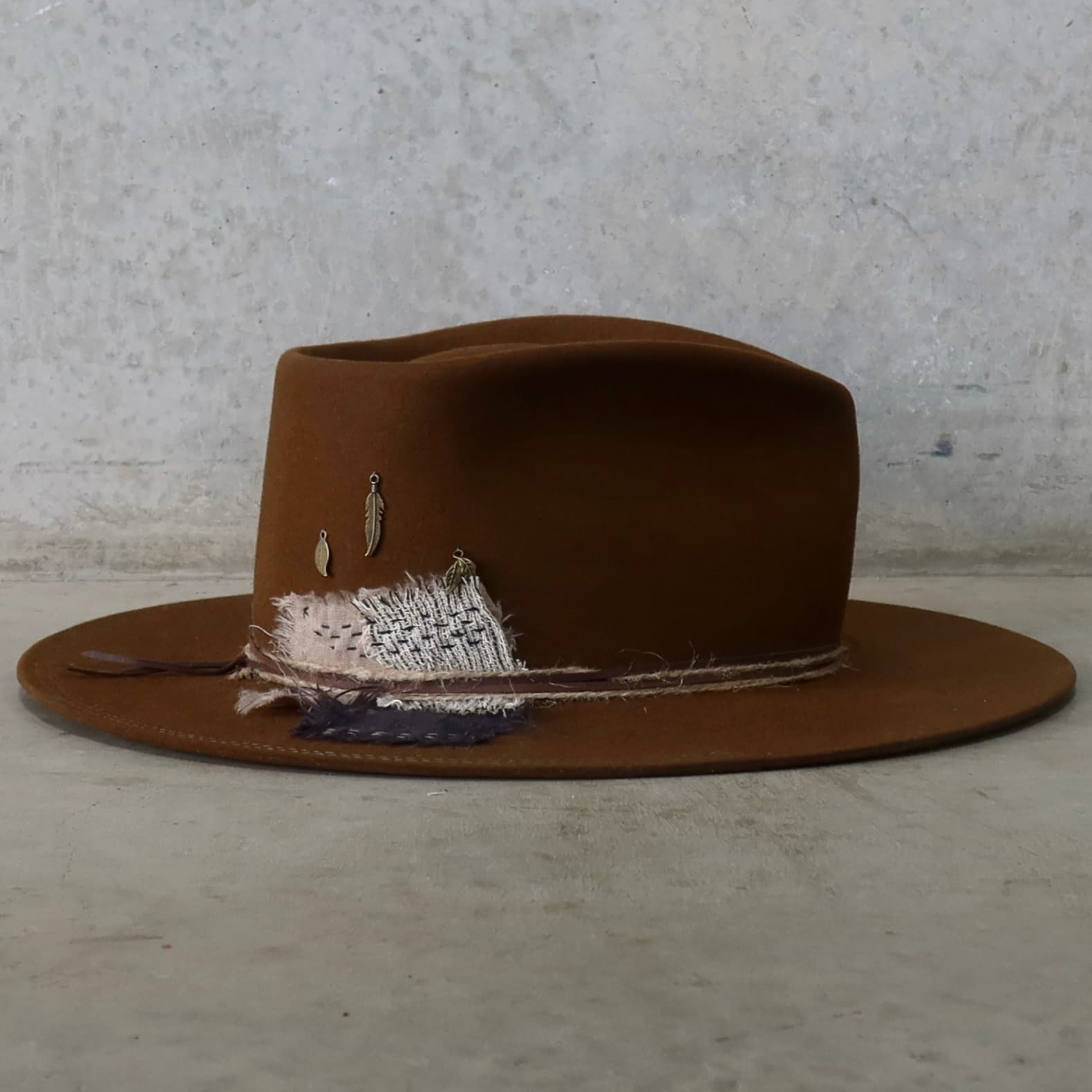 Right side view of the caramel felt hat George Limited Edition by PHYLLi Designs with Wabi Sabi linen patchwork, bronze feather and leaf charms, and leather string with twine wraps.
