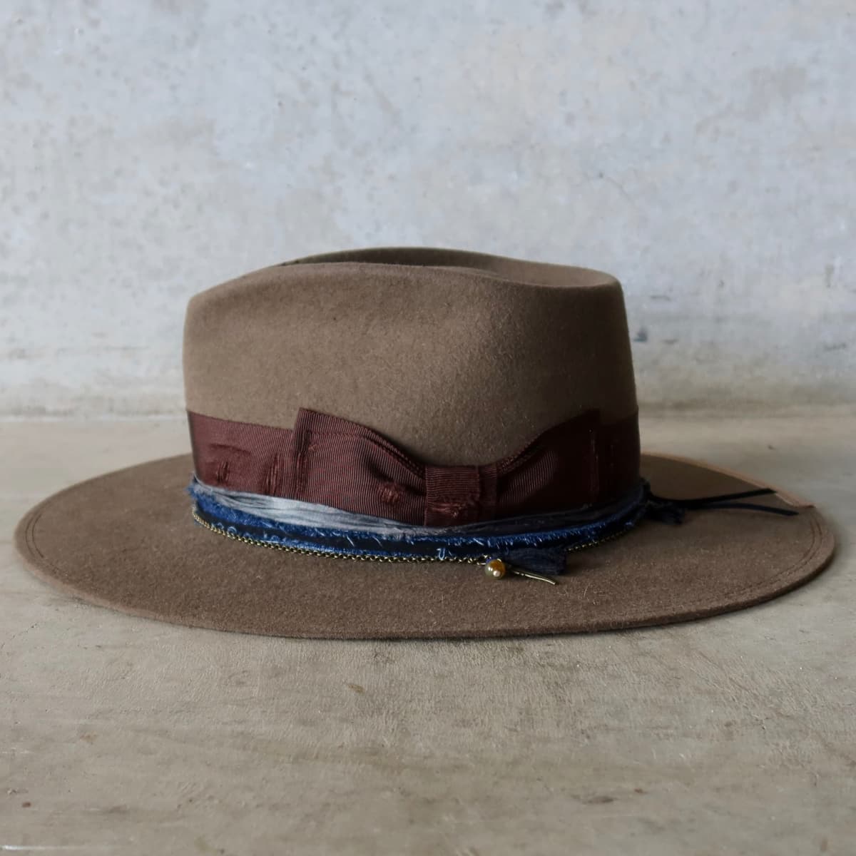 Left side view of the Dirty Olive felt hat Grove by PHYLLi Designs with navy denim and sari silk trim, bronze crown chain and charm cluster.
