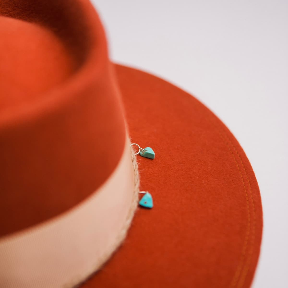 Close up detail of the Howlit felt hat showing turquoise stone charms set along the twine trim above the brim.