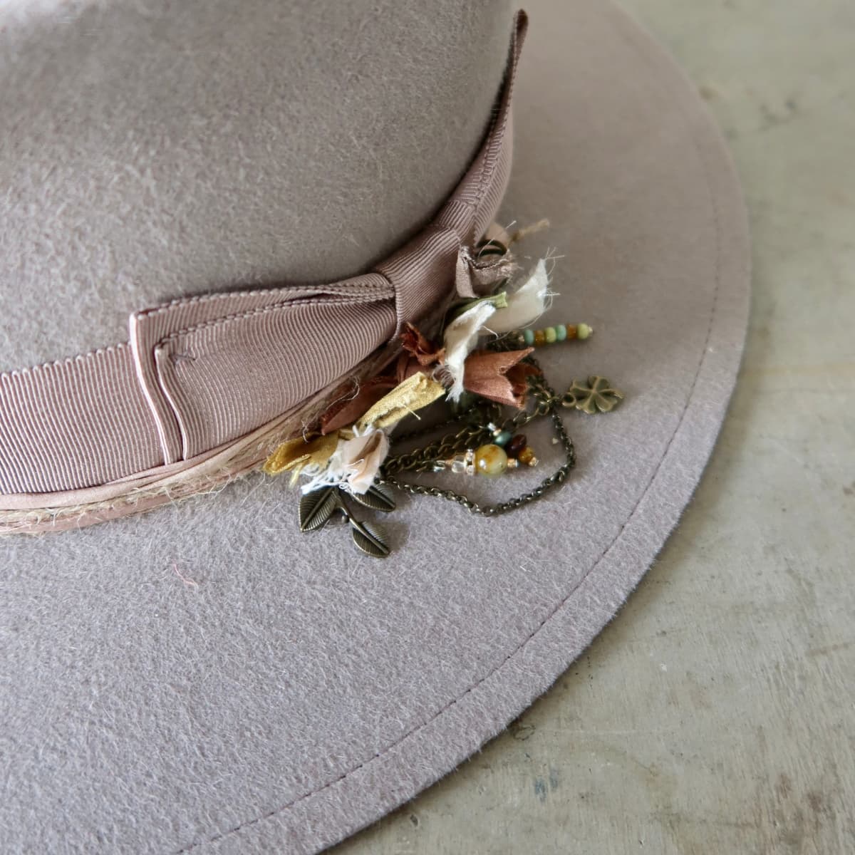 Close up detail of the Huskisson felt hat showing antique bronze chunky hat pin with sari silks, charms and beads.
