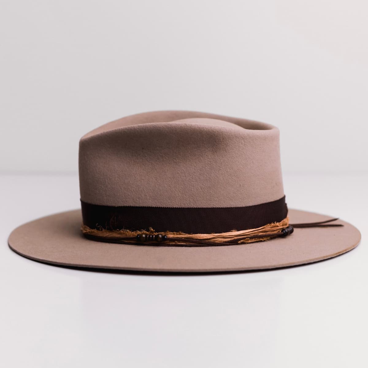 Left side view of the Sahara felt hat Hyndman by PHYLLi Designs with chocolate suede string and wooden bead detailing.