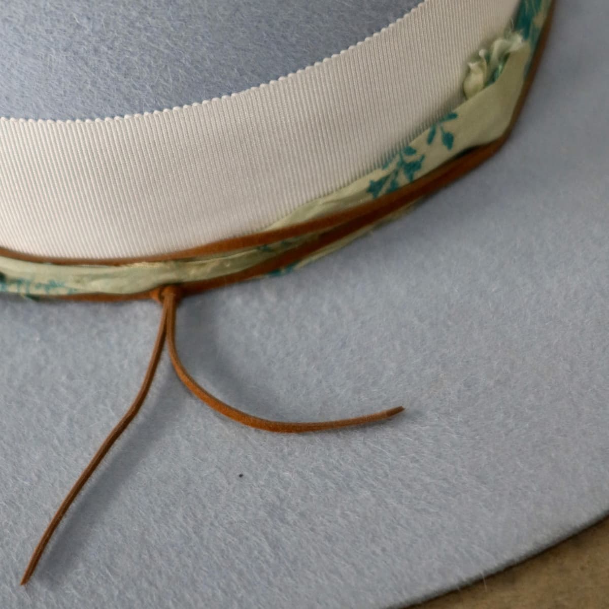 Close up detail of the Jarvis felt hat showing blue and teal patterned sari silk trim with tan suede string tie.
