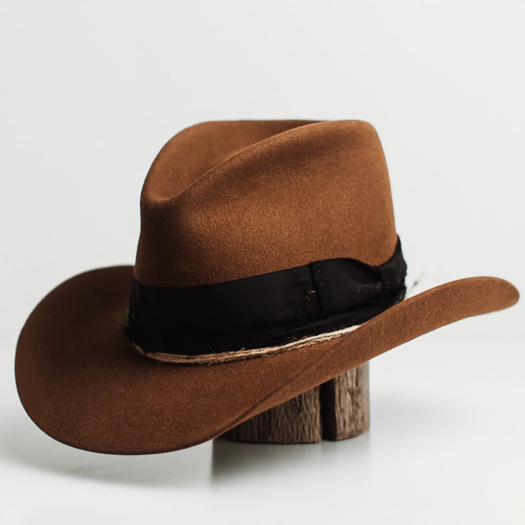 Front left angle of the Jersey caramel felt cowboy hat by PHYLLi Designs with distressed black grosgrain band and twine wraps with recycled glass beads.