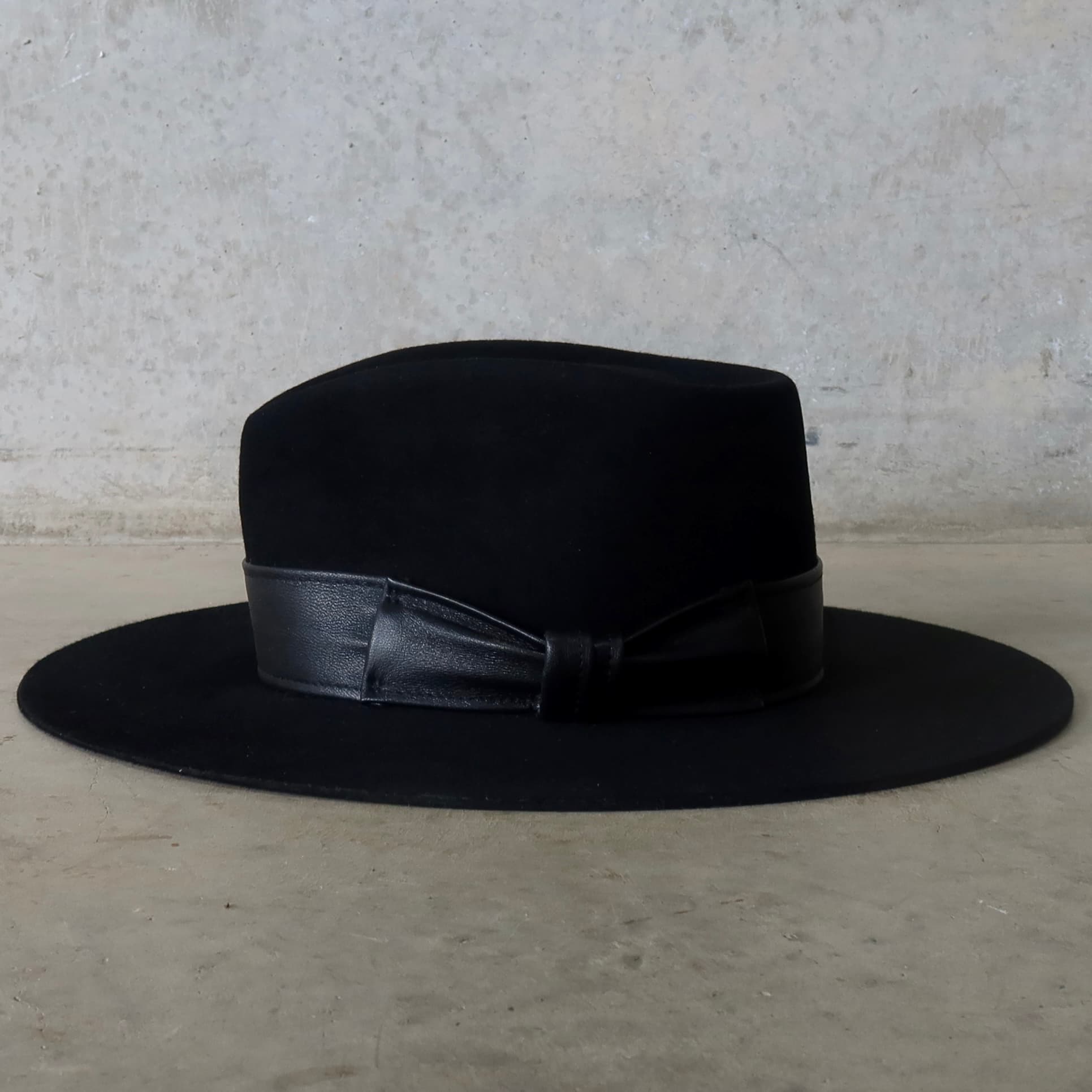 Left side view of the black felt hat Kirrilee by PHYLLi Designs with sheepskin leather bow band.