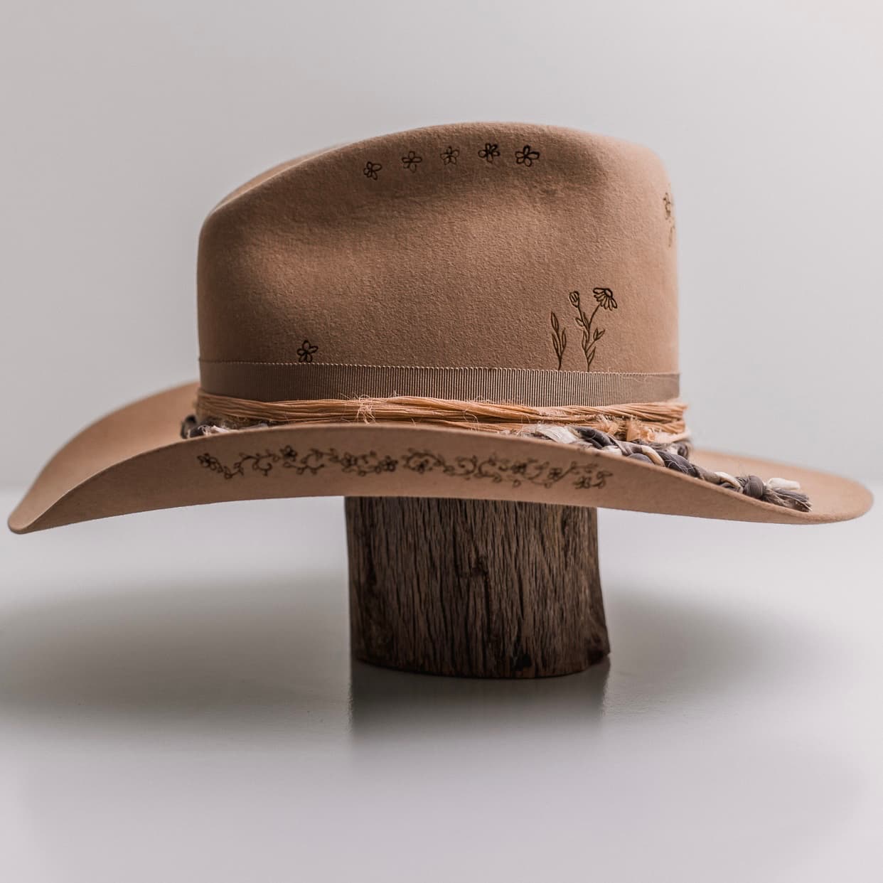 Left side view of the camel felt cowboy hat La Fleurs by PHYLLi Designs with braided sari silk trim and burnt floral crown and brim branding.