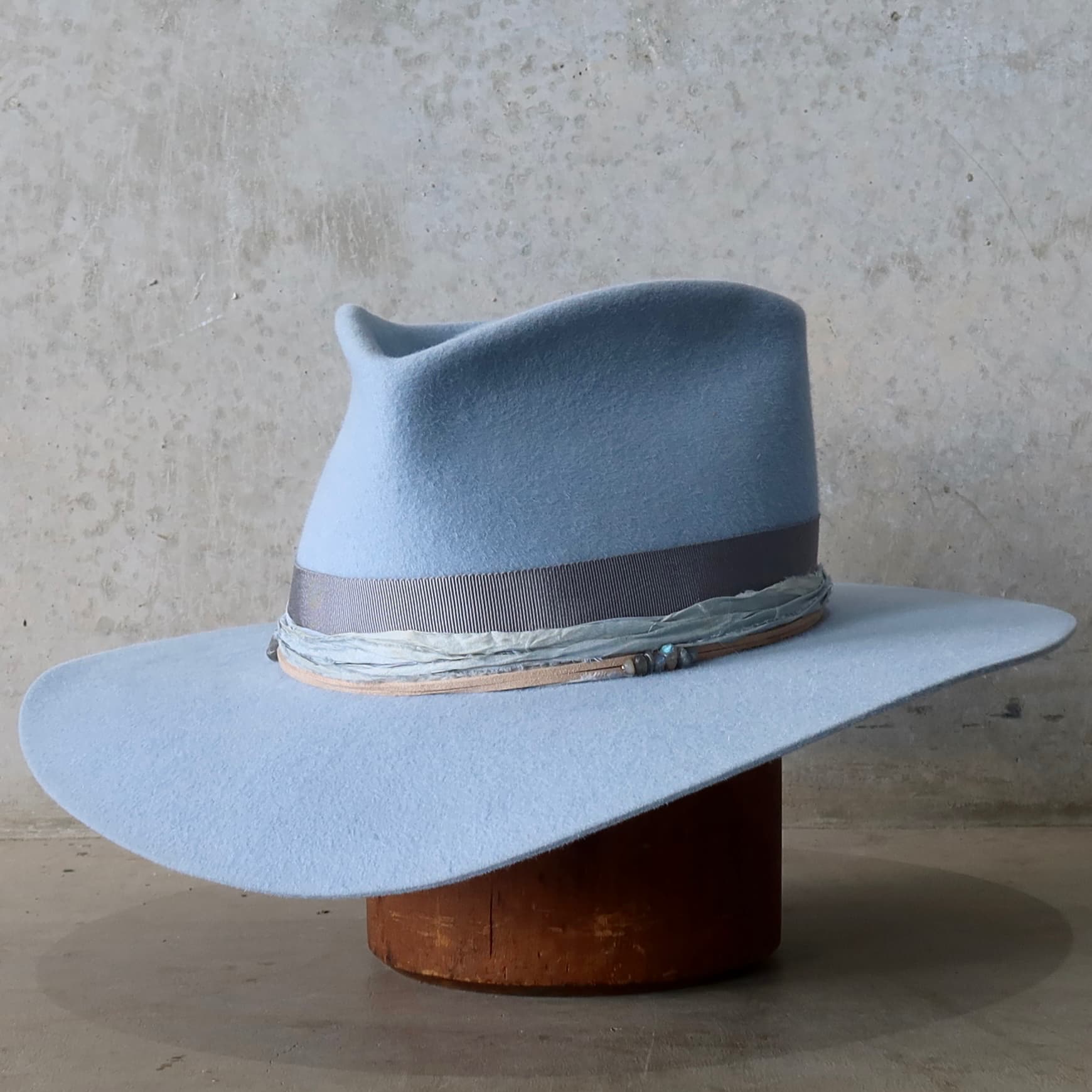 Front left angle of the La Journee Crystal Blue felt hat by PHYLLi Designs with cement grosgrain band and storm sari silk trimming.