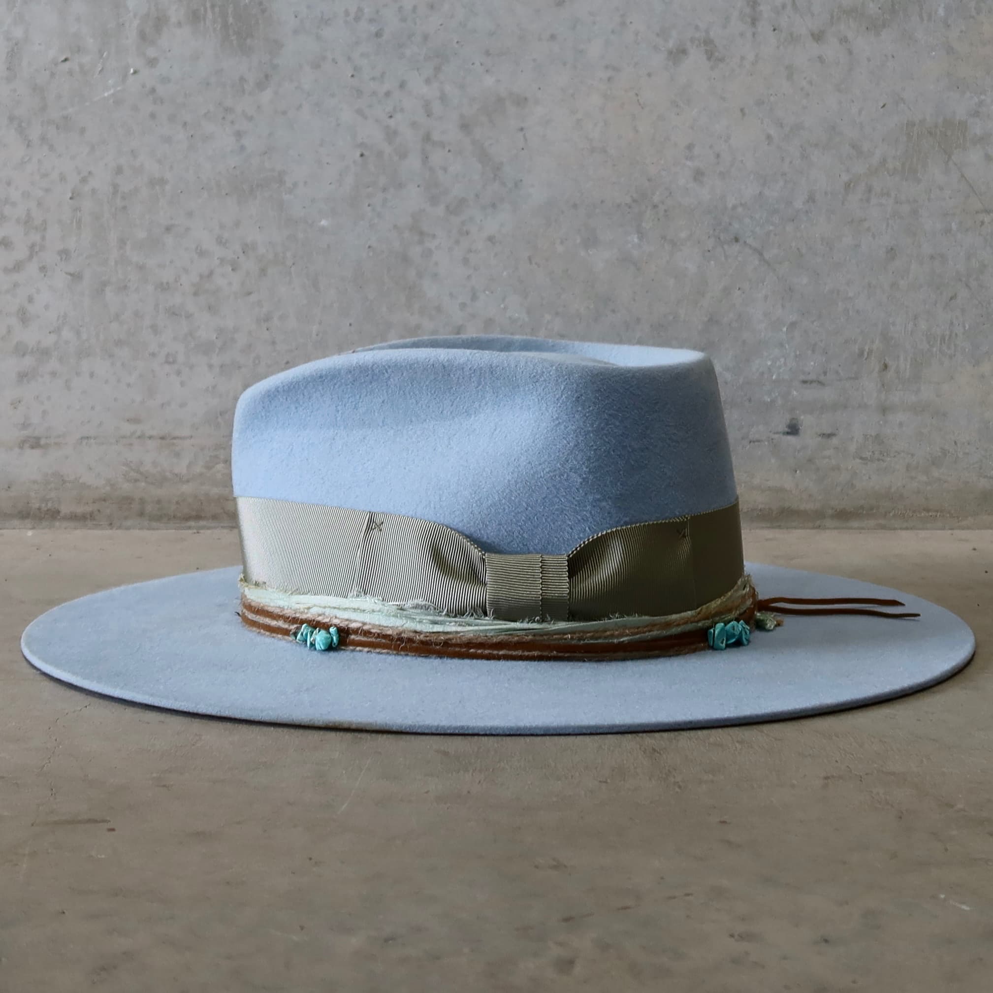 Left side view of the crystal blue felt hat Lagoon by PHYLLi Designs with oil green grosgrain band and layered twine and suede trims.