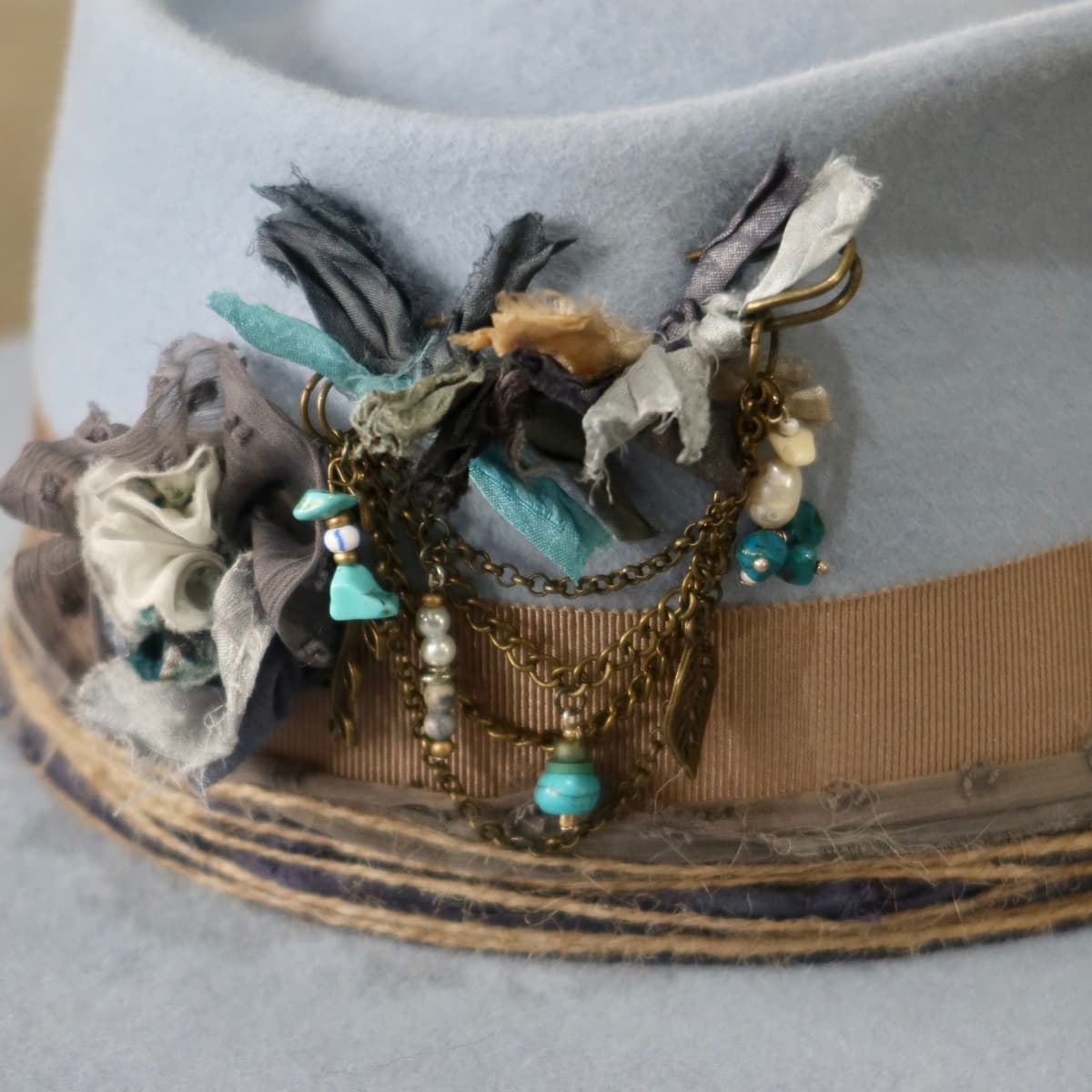Close up detail of the Louise felt hat showing bronze chunky hat pin with sari silks, charms and turquoise bead.