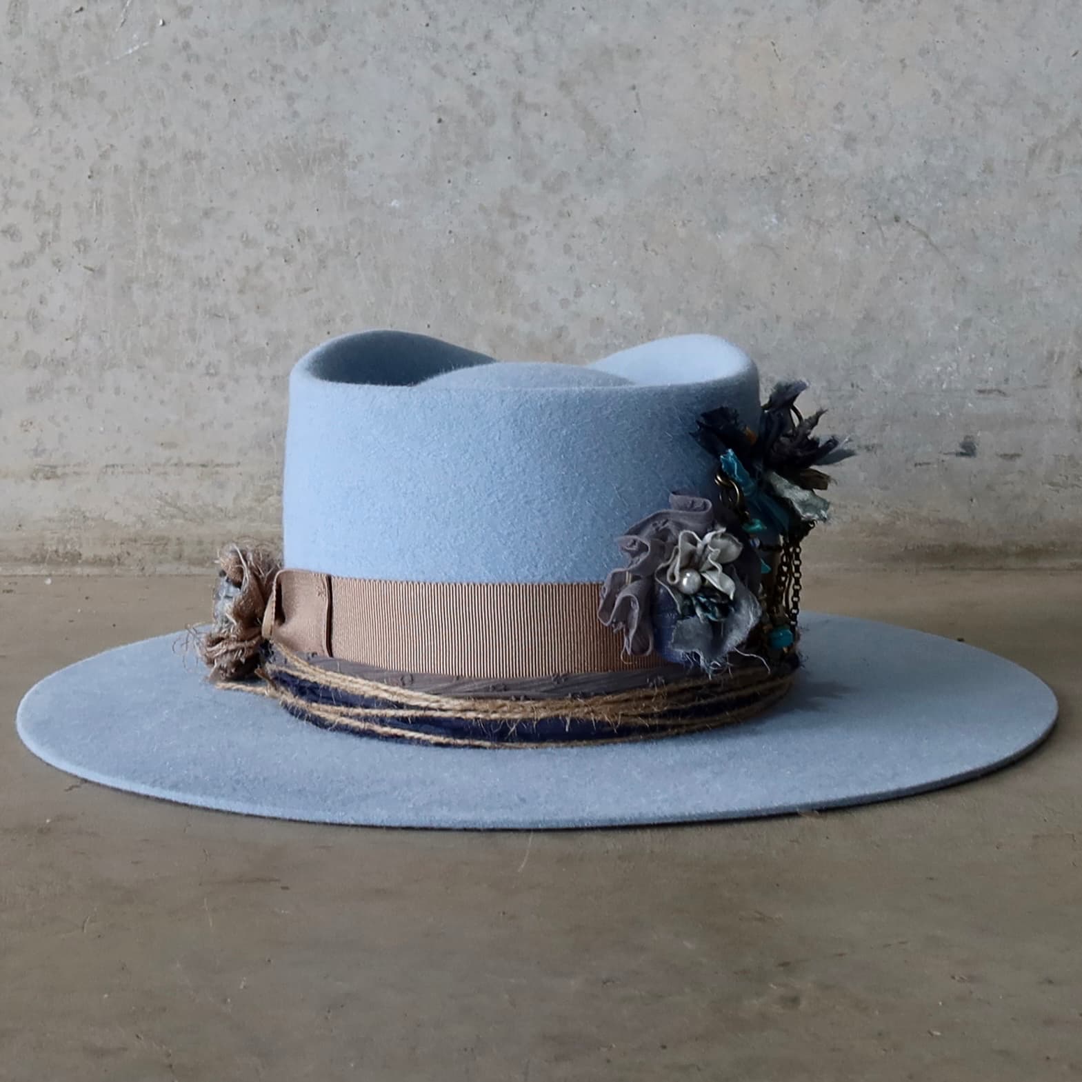 Back view of the crystal blue felt hat Louise by PHYLLi Designs featuring taupe Japanese grosgrain band, sari silks four twine wraps and sari silk Lapel Bloom detail.