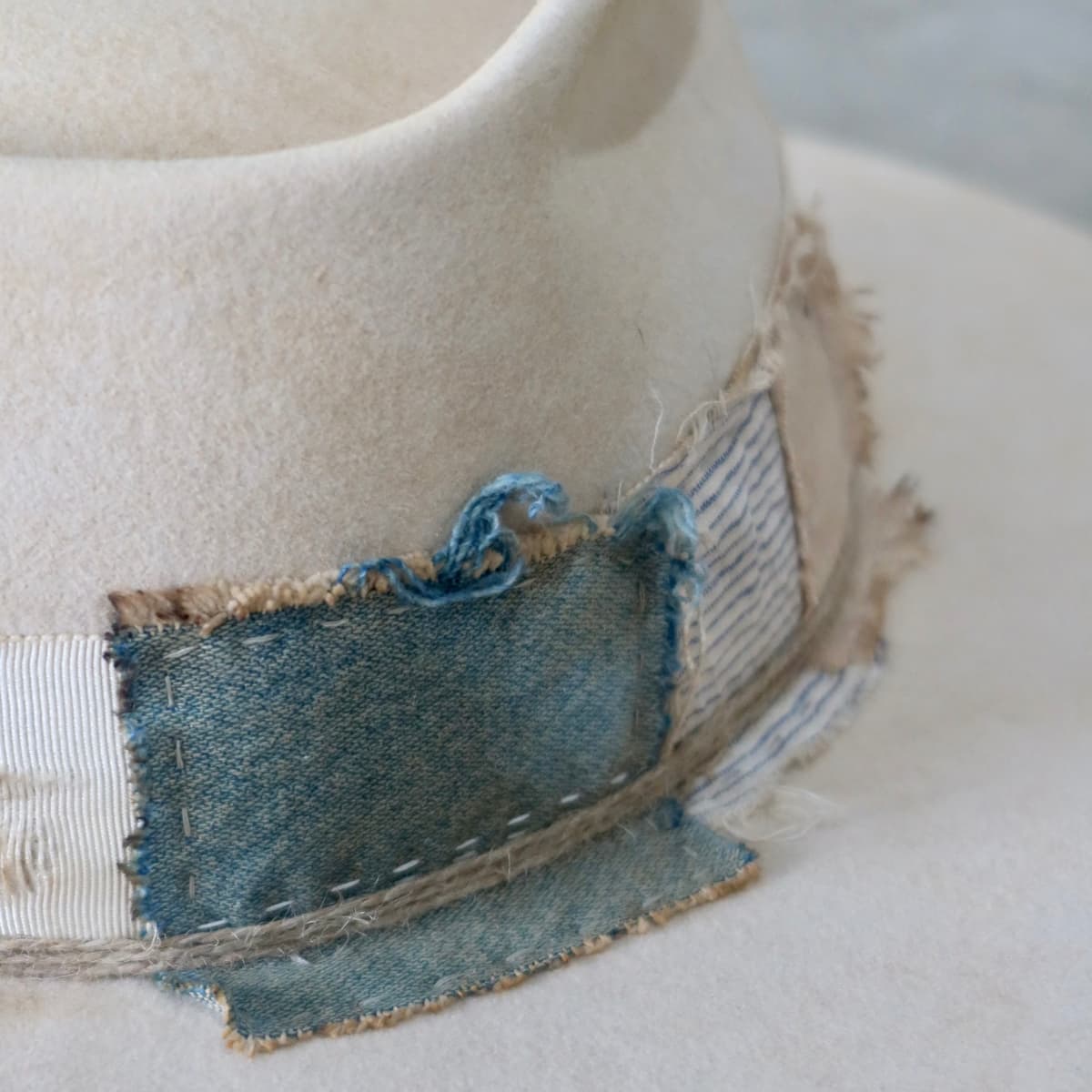 Close up detail of the Lucille Limited Edition felt hat showing worn indigo denim patch and raw stitched edges.