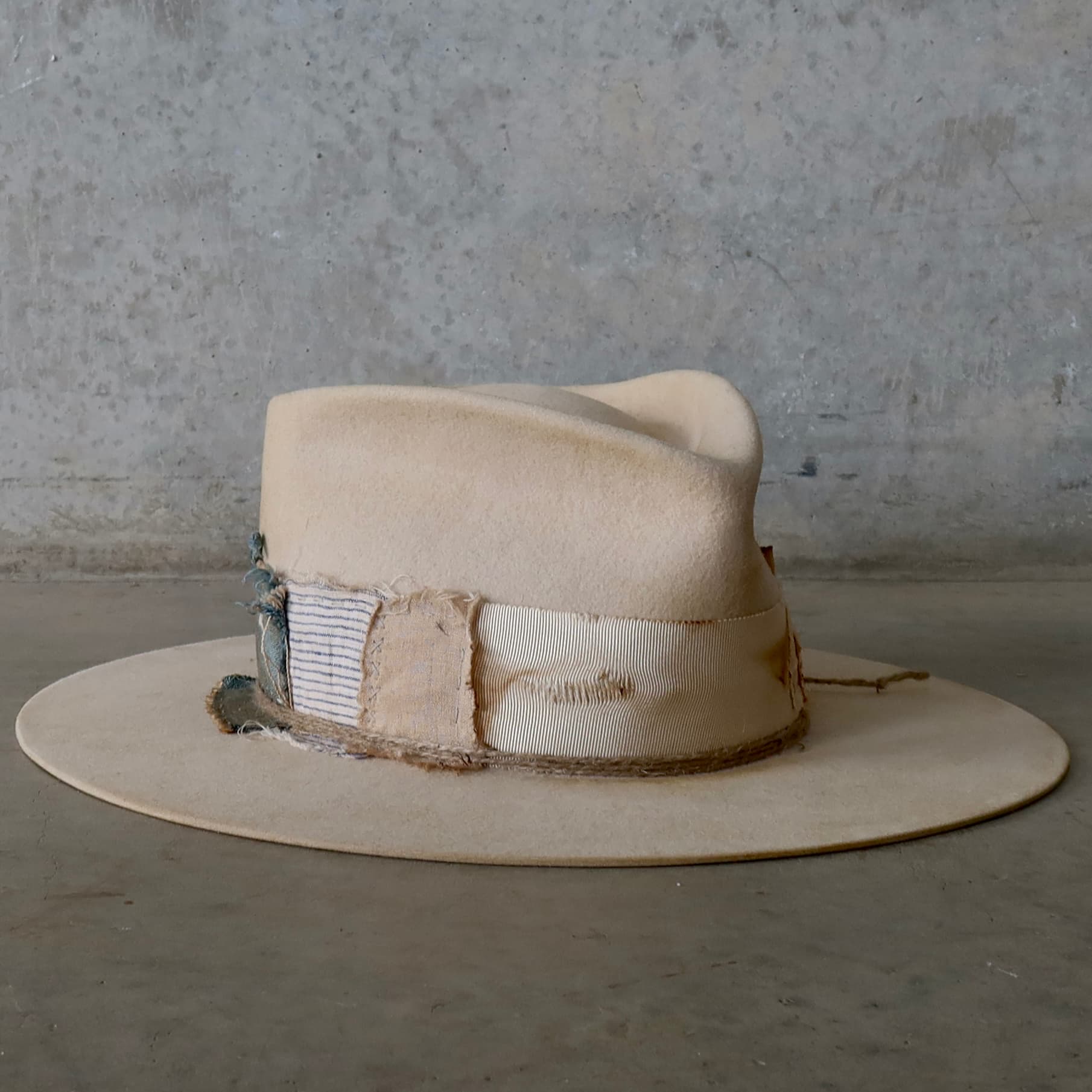 Front right angle of the beige felt hat Lucille Limited Edition by PHYLLi Designs with distressed ivory grosgrain bow band, patchwork trims and twine wraps.