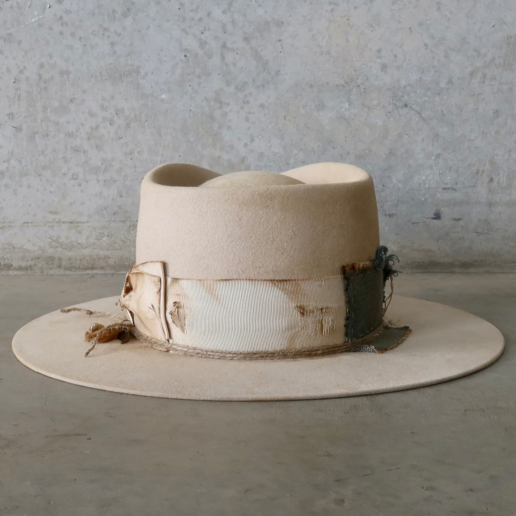 Back view of the beige felt hat Lucille Limited Edition by PHYLLi Designs featuring distressed grosgrain bow band and hand-stitched patchwork trims.