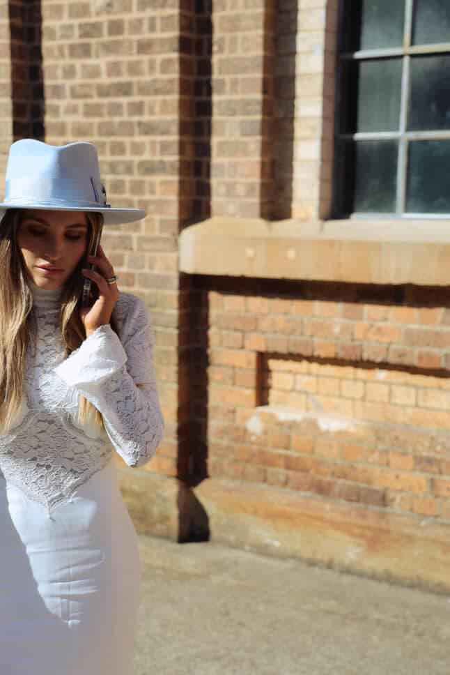 Model wearing the Crystal Blue felt hat Lucinda by PHYLLi Designs with cornflower grosgrain bow band while walking outdoors in a city setting.