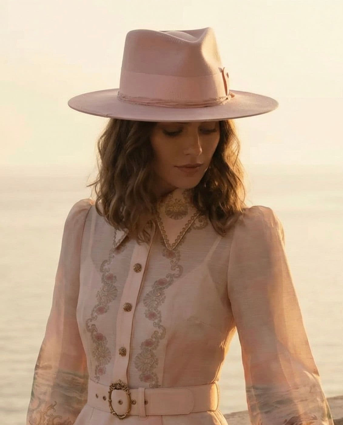Woman wearing the Baby Pink felt hat Lucinda Bloom by PHYLLi Designs with salmon grosgrain bow band at the seaside during golden hour.