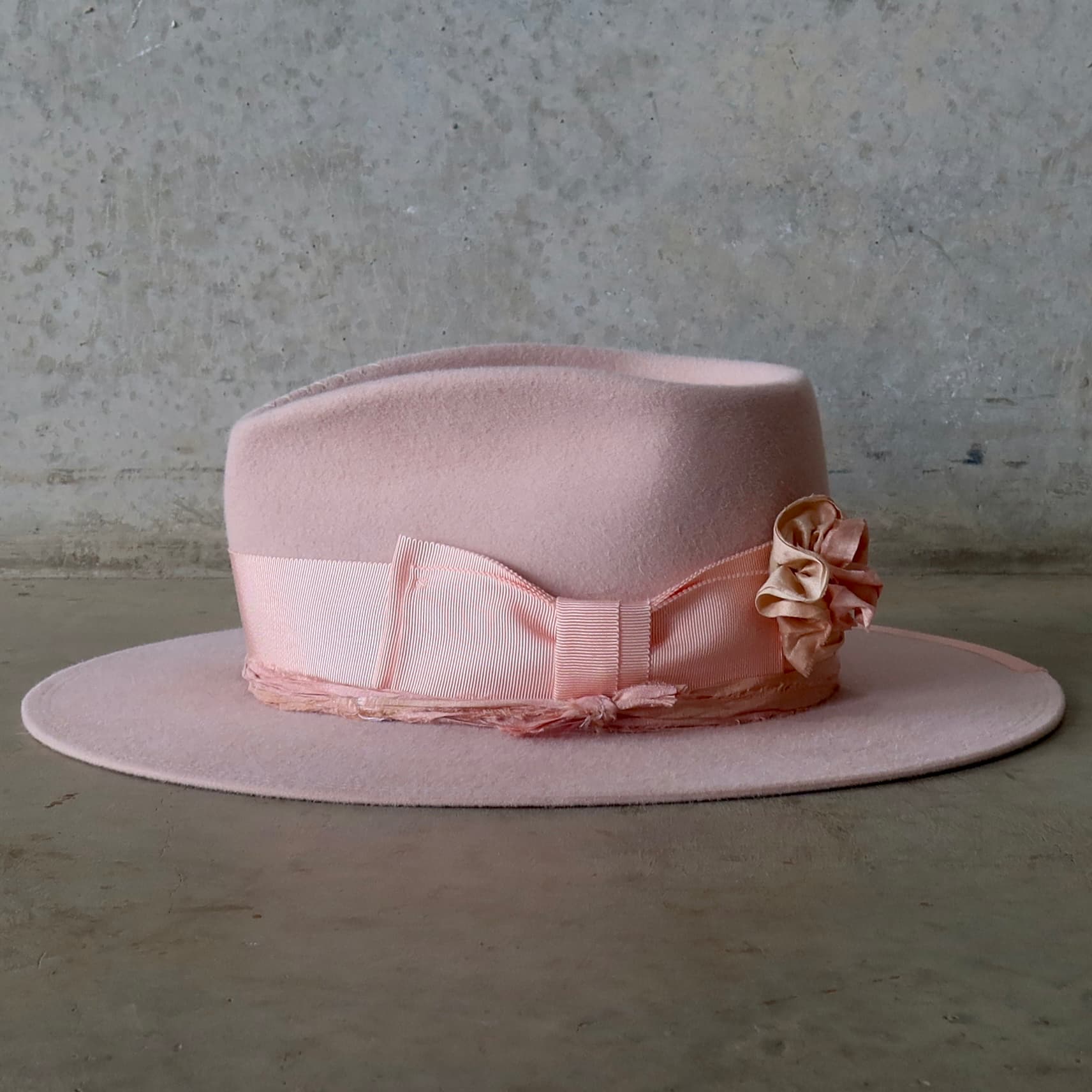 Left side view of the Baby Pink felt hat Lucinda Bloom by PHYLLi Designs with salmon grosgrain band and removable sari silk lapel bloom.