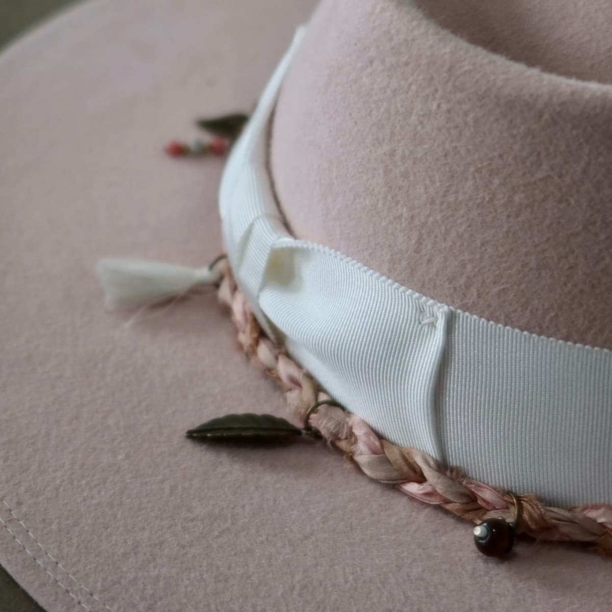 Close up detail of the Lucky Charm felt hat showing Charm Plait in pink sari silks with bronze leaf charm and bead pendants.