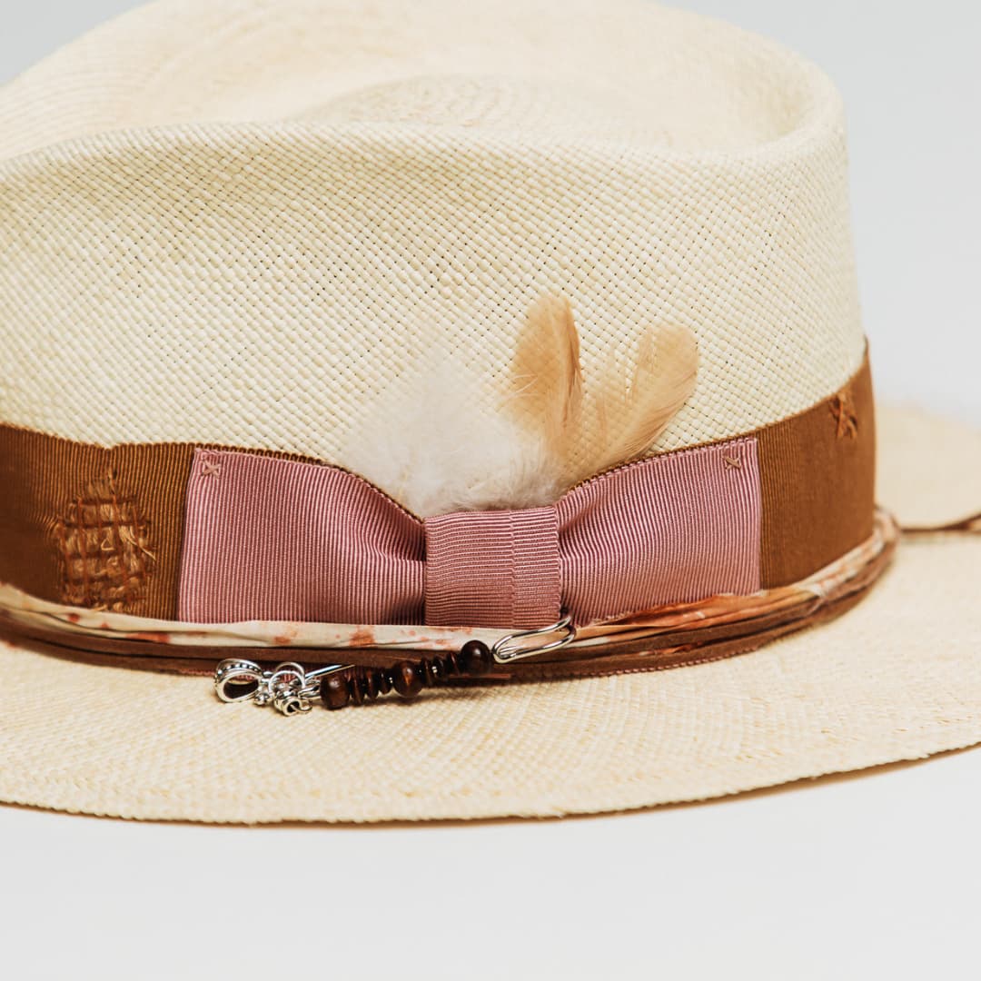 Detail of Malibu Panama hat showing Rose grosgrain bow, tan chicken feathers and silver hat pin with wooden beads and pendant charms.