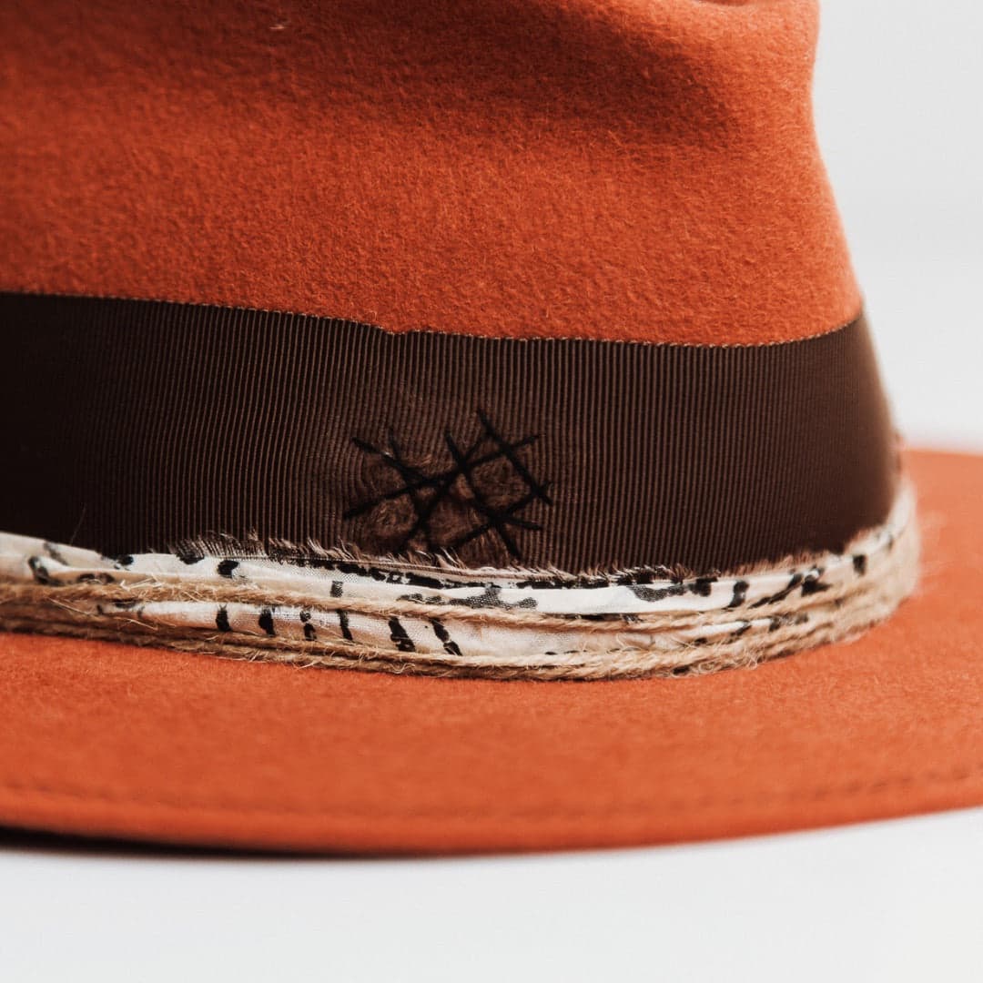 Close up detail of the Marrakech spiced pumpkin felt hat by PHYLLi Designs showing distressed praline grosgrain band with black darned patch and black and white sari silk trim.