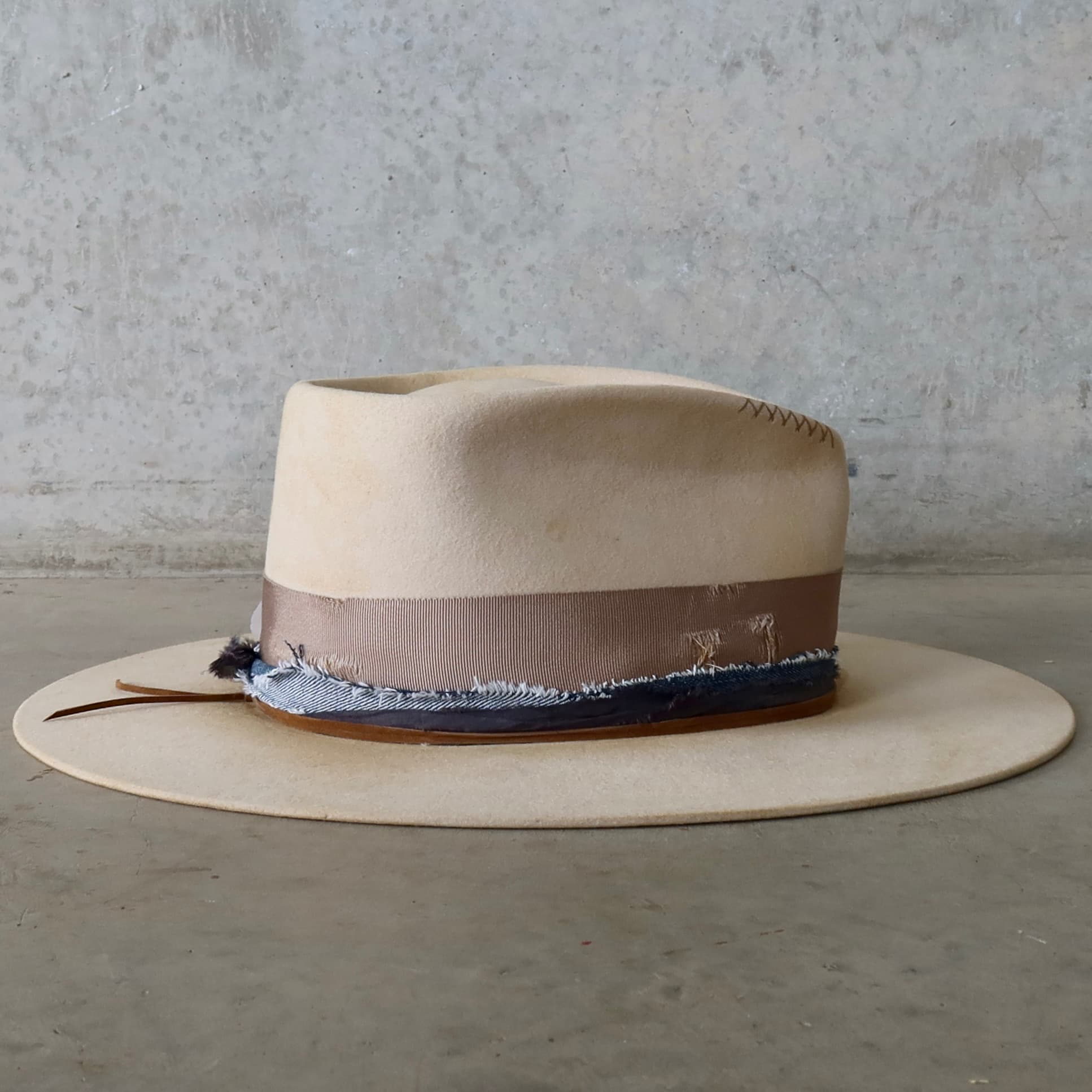 Right side view of the beige distressed felt hat McVeigh by PHYLLi Designs with feather bunch and navy sari silk and denim trimming.