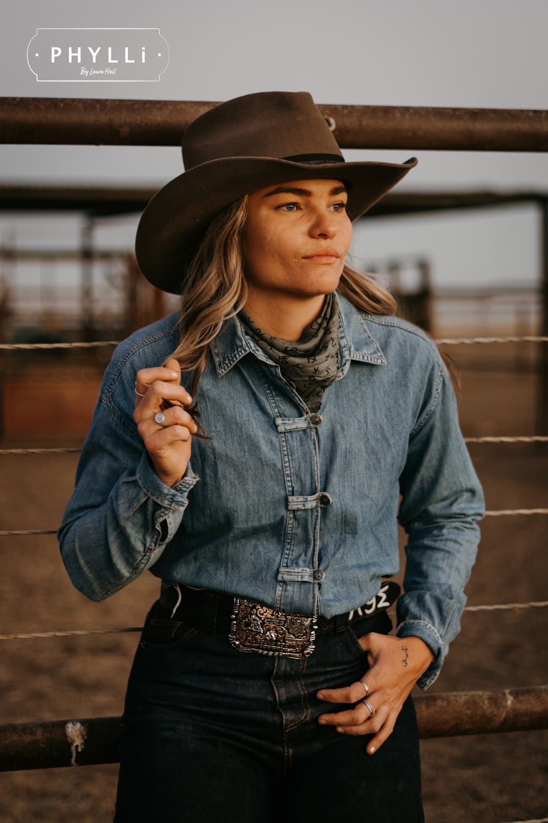 Woman wearing the Midnight Cowboy dirty olive felt cowboy hat by PHYLLi Designs with black Japanese grosgrain ribbon band and buffalo leather tieback hat band in rural cattle yards.