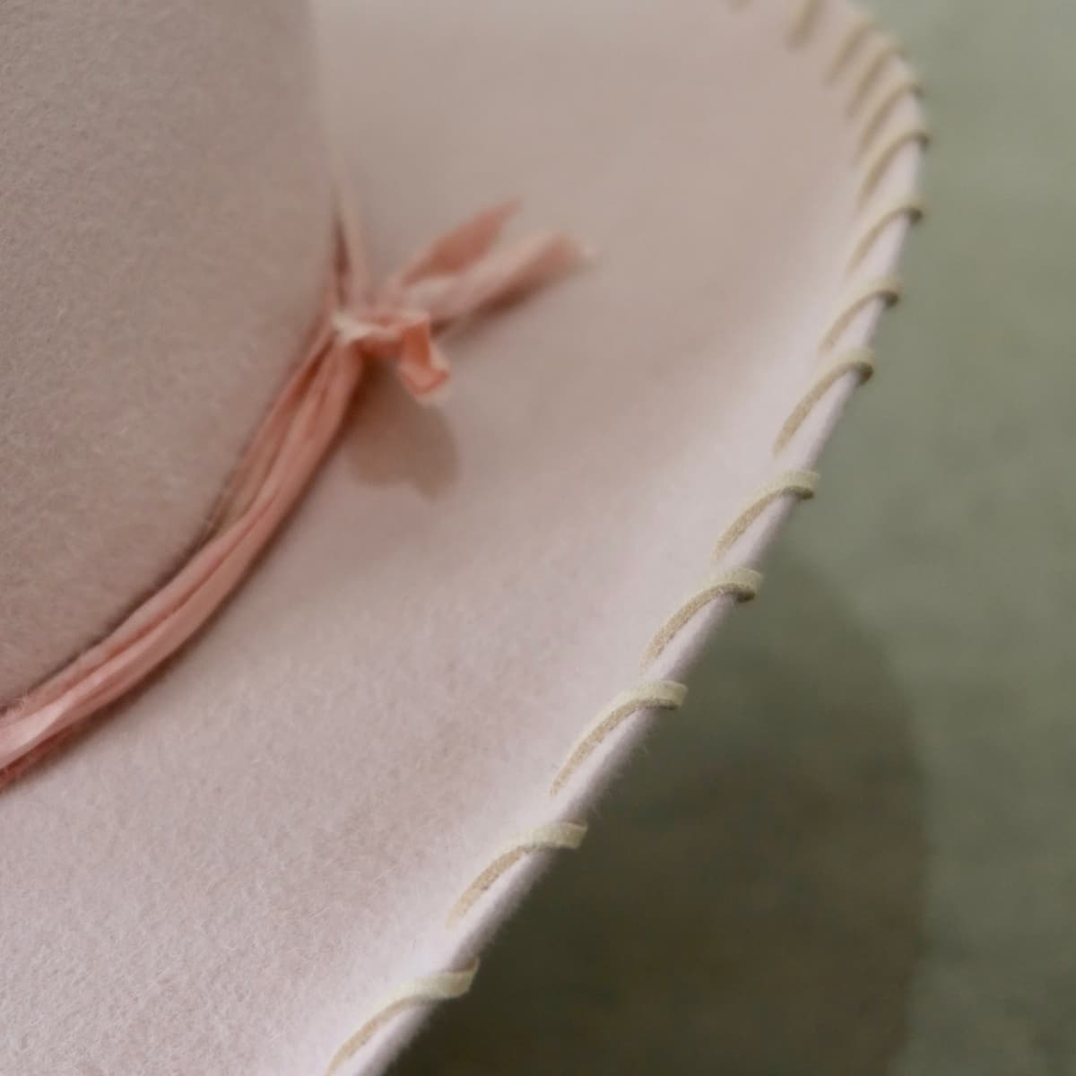 Close up detail of the Nevada cowboy hat showing nude suede brim lacing stitched through the baby pink felt brim with tonal silk yarn wraps at the crown.