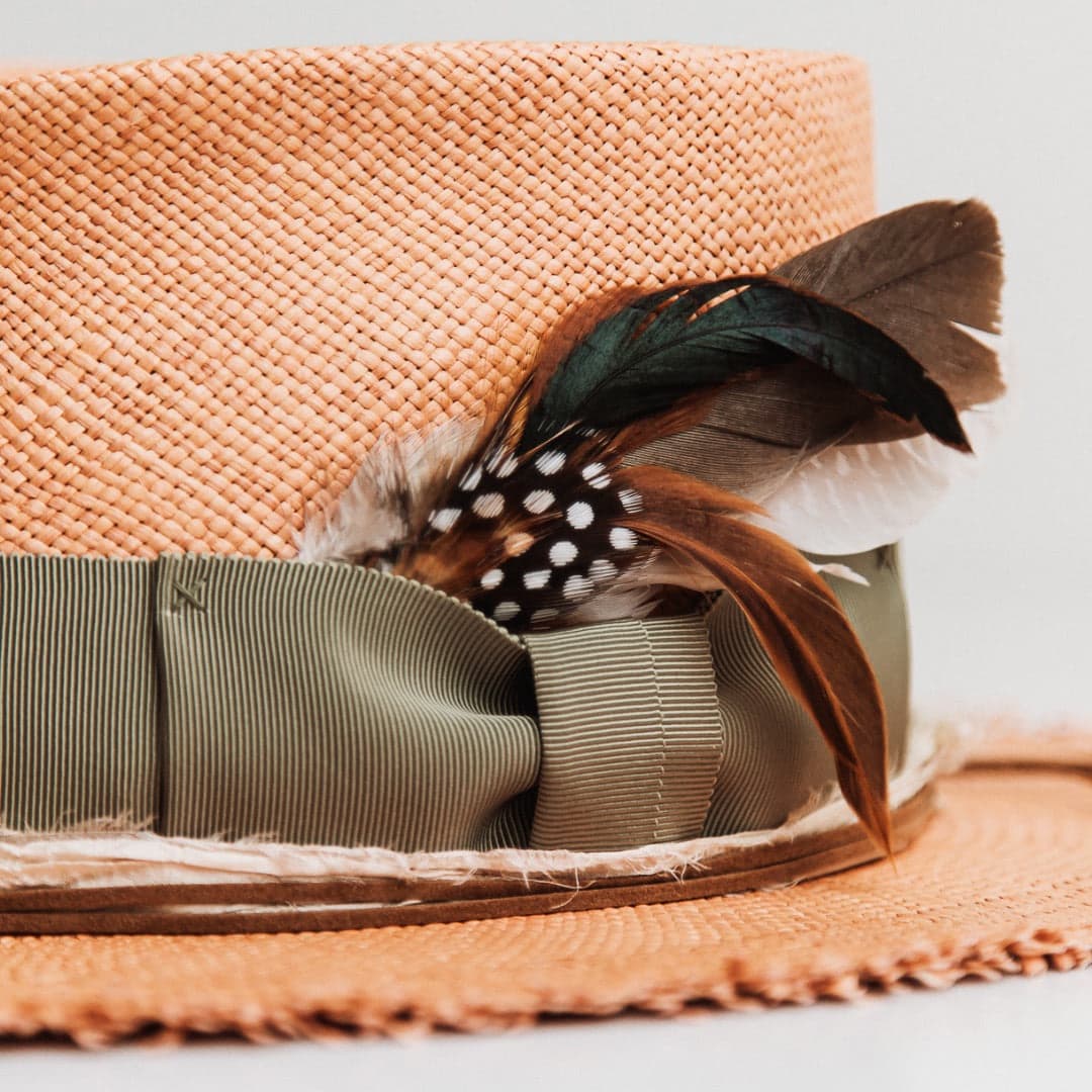 Close up detail of the Nim Panama biscuit Panama hat by PHYLLi Designs showing the oil green Japanese grosgrain bow band and assorted fallen feather bunch.