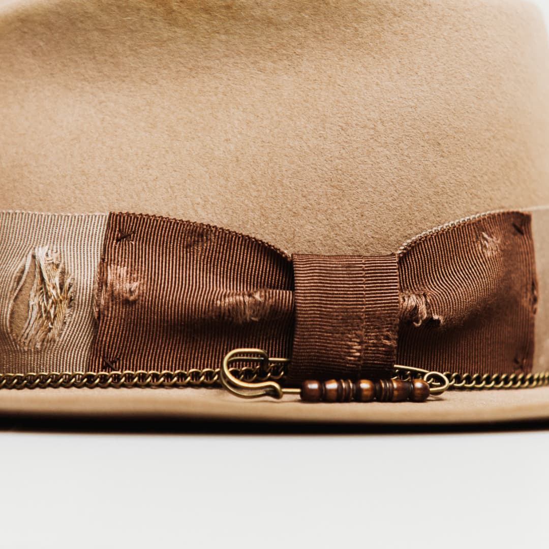 Close up detail of the Normie felt hat showing chocolate bow, bronze crown chain and bone beaded hat pin.