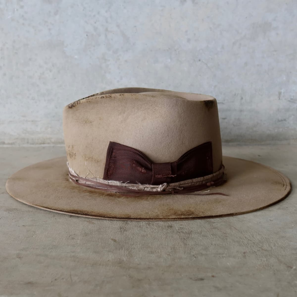 Left side view of the Sahara distressed felt hat Old Joe by PHYLLi Designs with distressed dark brown Japanese grosgrain floating double bow.