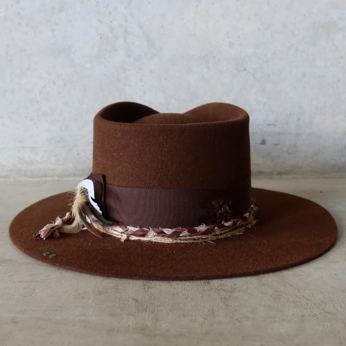 Back view of the Chocolate felt hat Palmer Limited Edition by PHYLLi Designs featuring fallen feather bunch and plaited sari silk trim.
