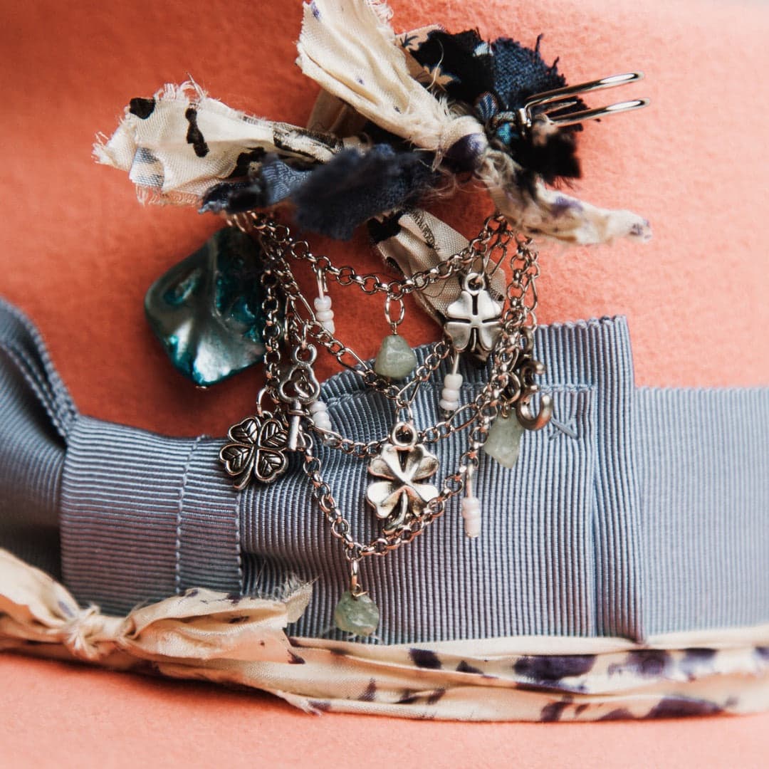 Close up detail of the Pāua felt hat showing chunky silver hat pin with charms, sari silk tassels and beads.