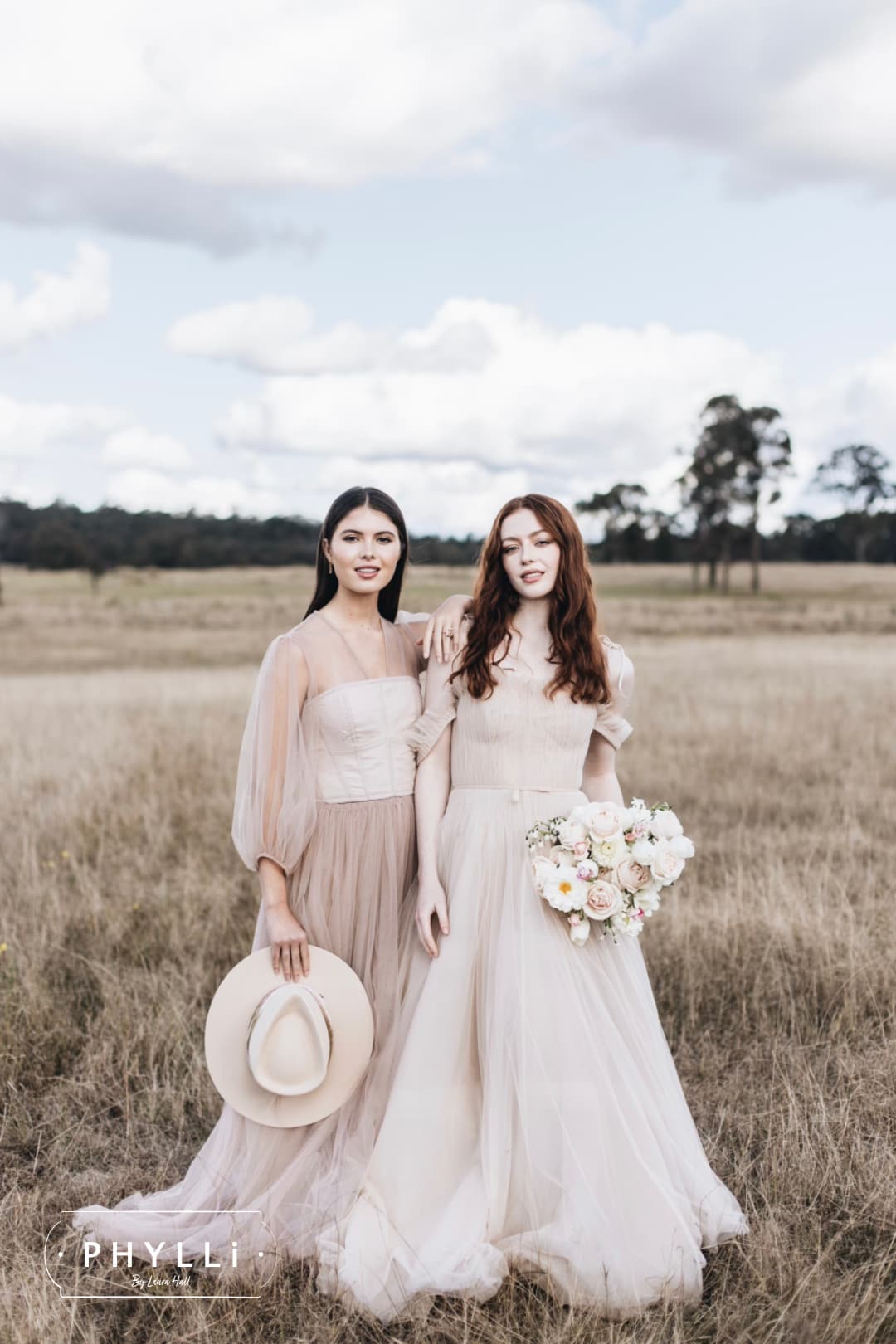 Brides in soft neutral dresses in a countryside setting with a beige felt bridal hat by PHYLLi Designs.