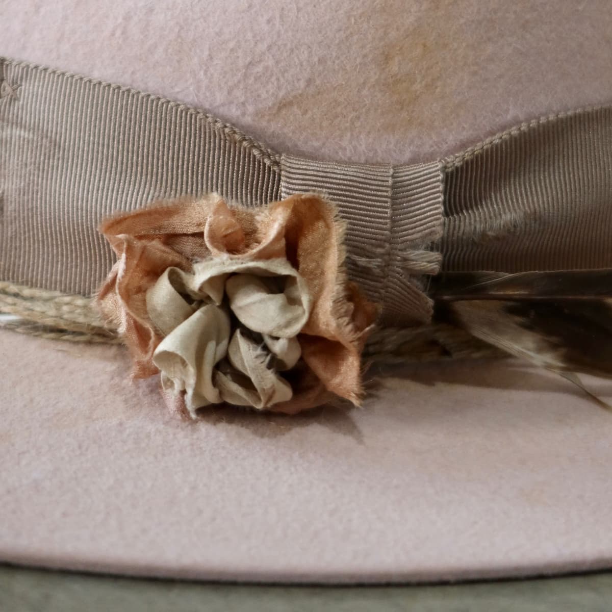 Right side view of the baby pink distressed felt hat Pink Bloom by PHYLLi Designs featuring sari silk lapel bloom, fallen hawk feather and distressed taupe grosgrain bow band.