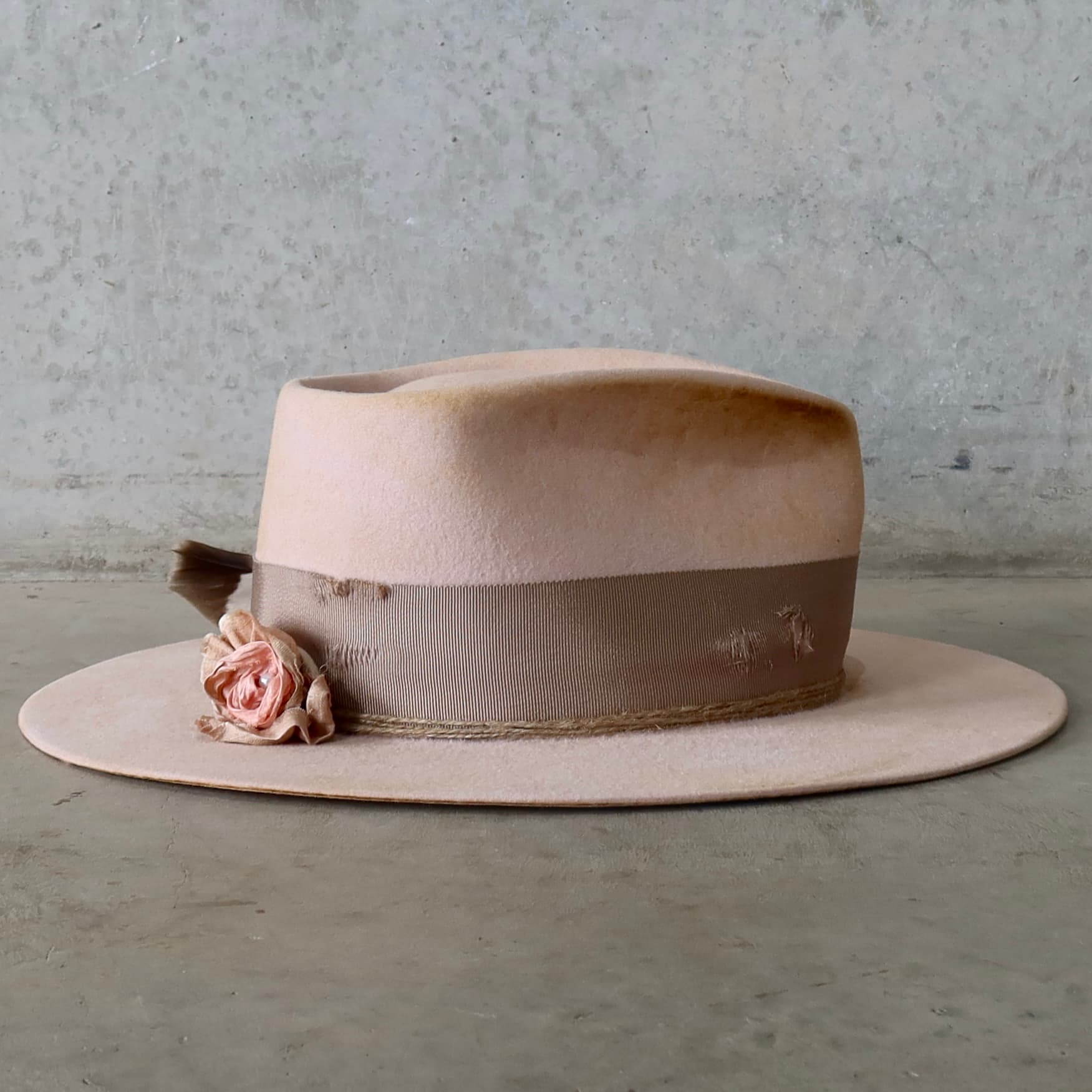 Right side view of the baby pink distressed felt hat Pink Bloom by PHYLLi Designs with sari silk lapel bloom, twine wraps and fallen hawk feather.