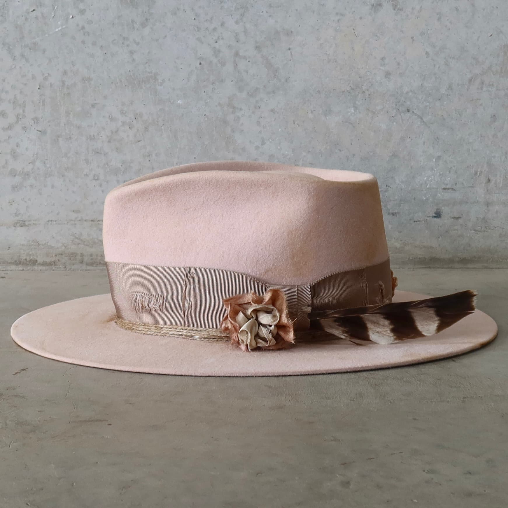 Left side view of the baby pink distressed felt hat Pink Bloom by PHYLLi Designs with sari silk lapel bloom and fallen hawk feather.