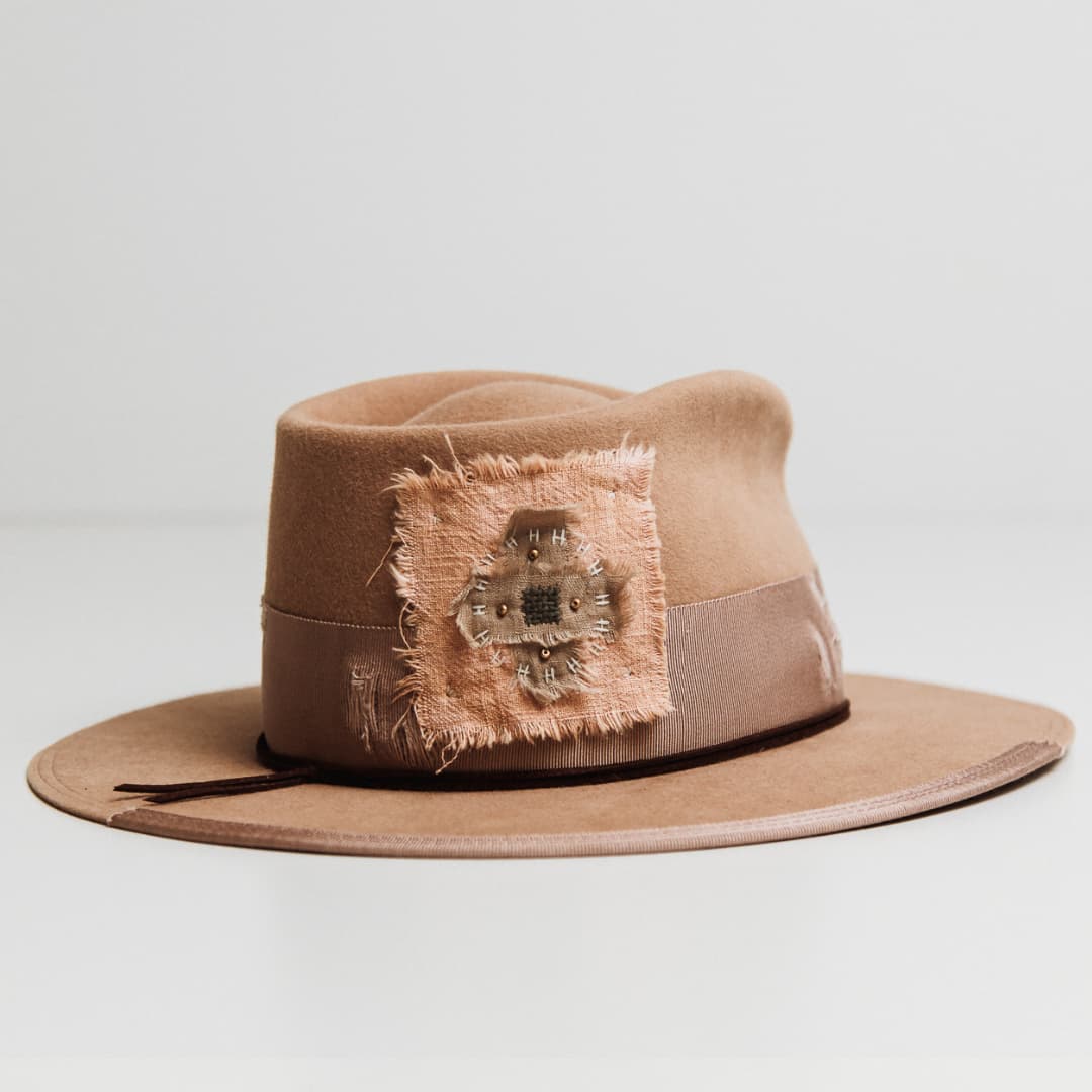 Back right angle of the Reiko camel felt hat by PHYLLi Designs featuring linen cross patterned patch with ivory stitching and gold beading.