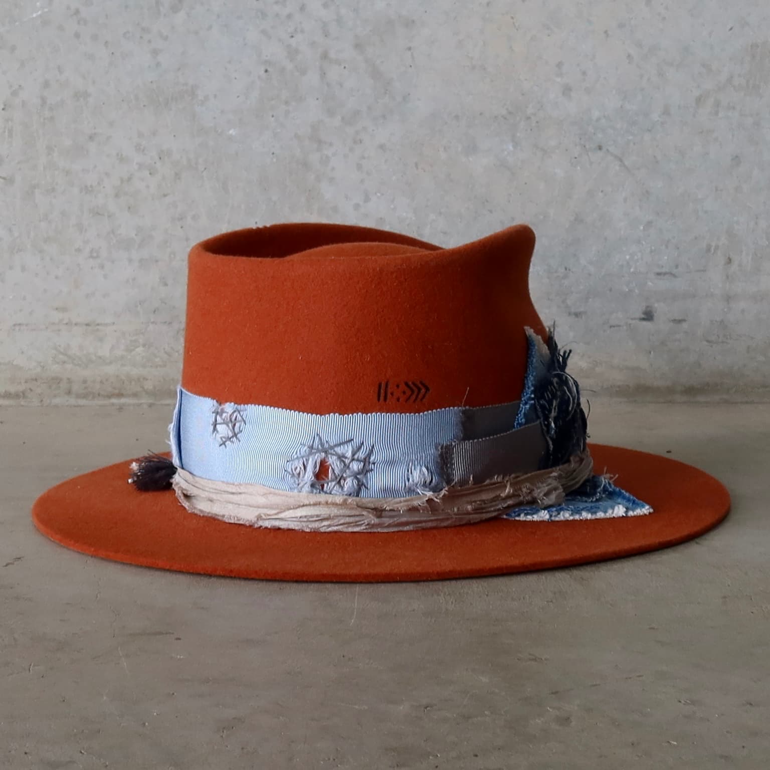 Back right angle of the Road Less Travelled spiced pumpkin felt hat by PHYLLi Designs with sari silk trim in Smoke and charm cluster with navy tassel.