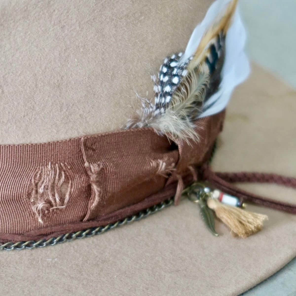 Close up of Roadie felt hat by PHYLLi Designs showing feather bunch and distressed grosgrain band.