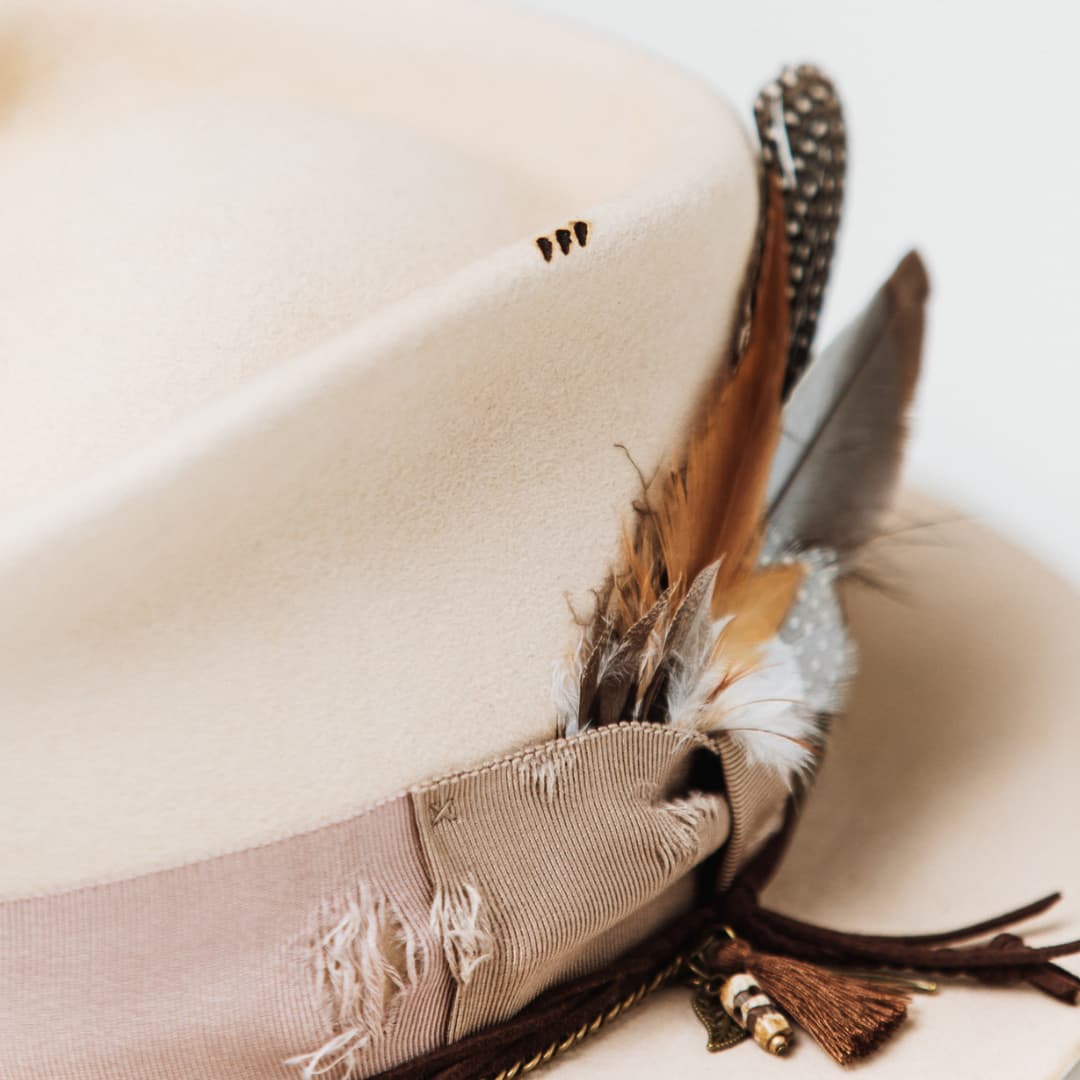 Close up detail of the Roadie felt hat showing feather cluster with leather ties and brass bead charm.