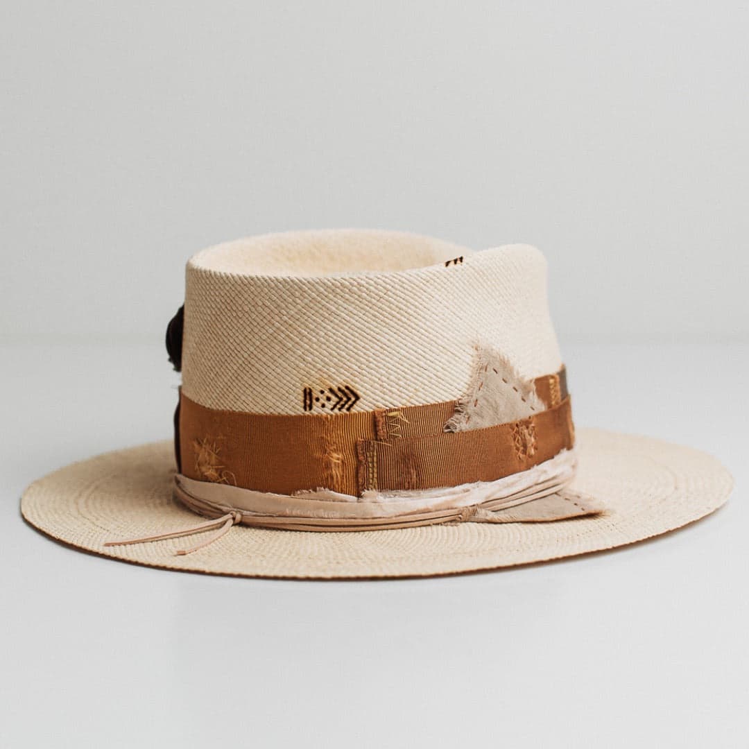 Back right angle of the Roadie Panama natural straw hat by PHYLLi Designs with charm cluster, fallen feather detail and burnt branded pattern.