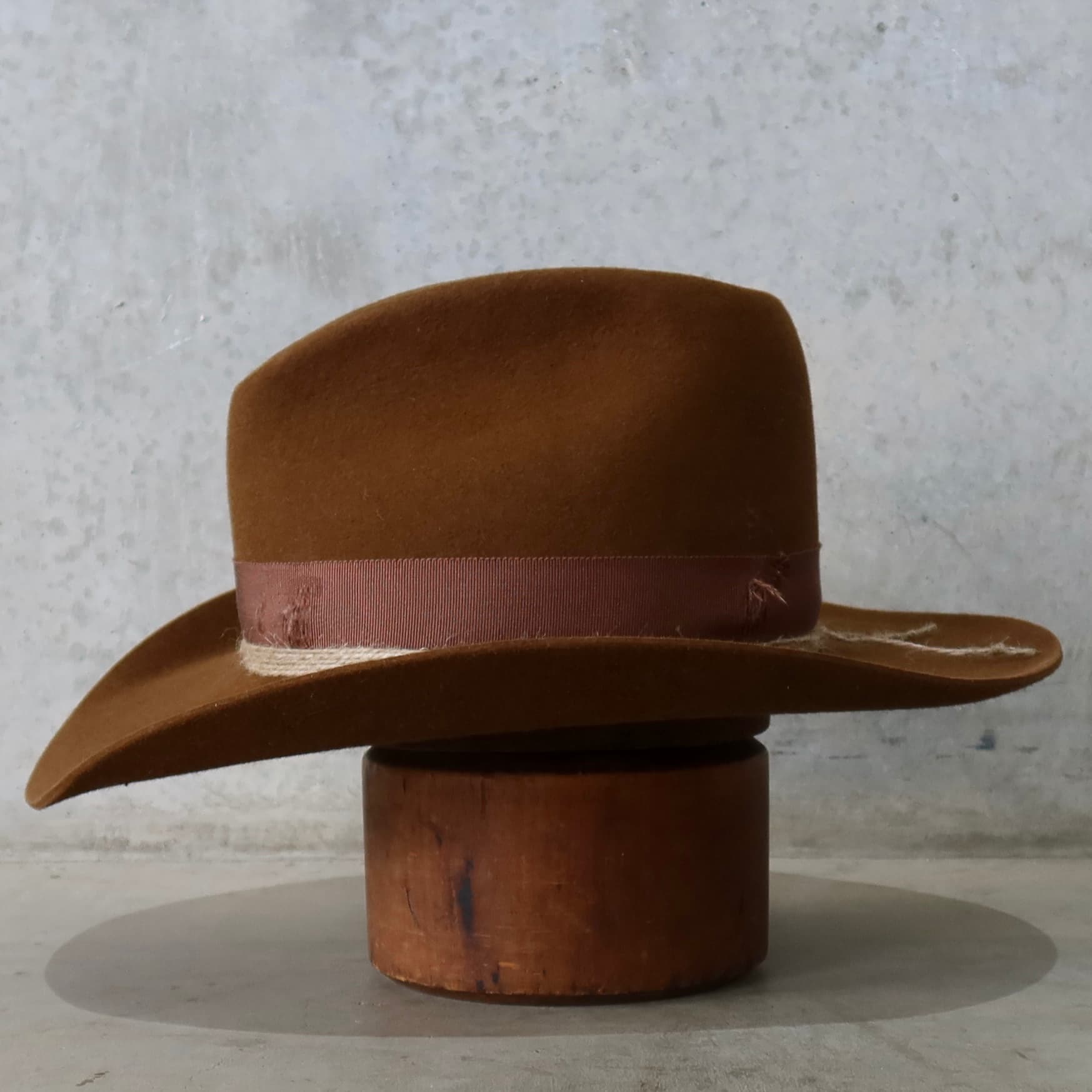 Left side view of the caramel cowboy hat Rue by PHYLLi Designs with distressed chocolate grosgrain band and turquoise beaded twine wraps.