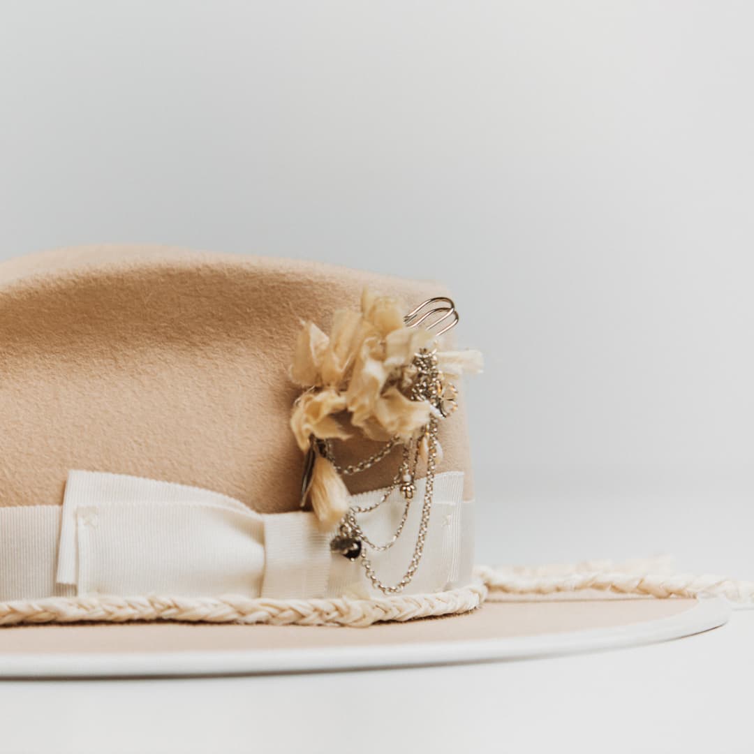 Close up detail of the Rue De Seine felt hat showing silver chunky hat pin with ivory tassel, sari silk fibres and chain charms.