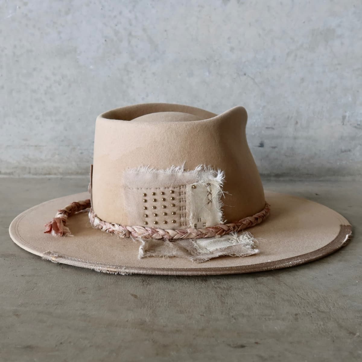 Back right angle of the sand distressed felt hat Ryoan Limited Edition by PHYLLi Designs featuring Wabi Sabi linen and silk patches with gold beading and plaited sari silk trimming.